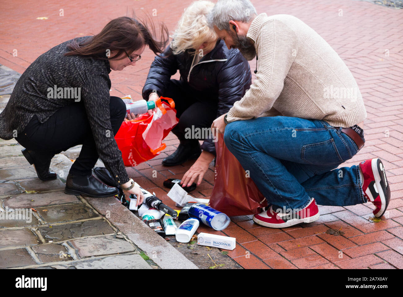 Der Käufer schnappt sich, um einkaufen zu gehen, nachdem sich eine nasse Papiertüte aufteilt und die heruntergefallenen Inhalte auf dem Straßenbelag fallen lässt. England Großbritannien (114) Stockfoto