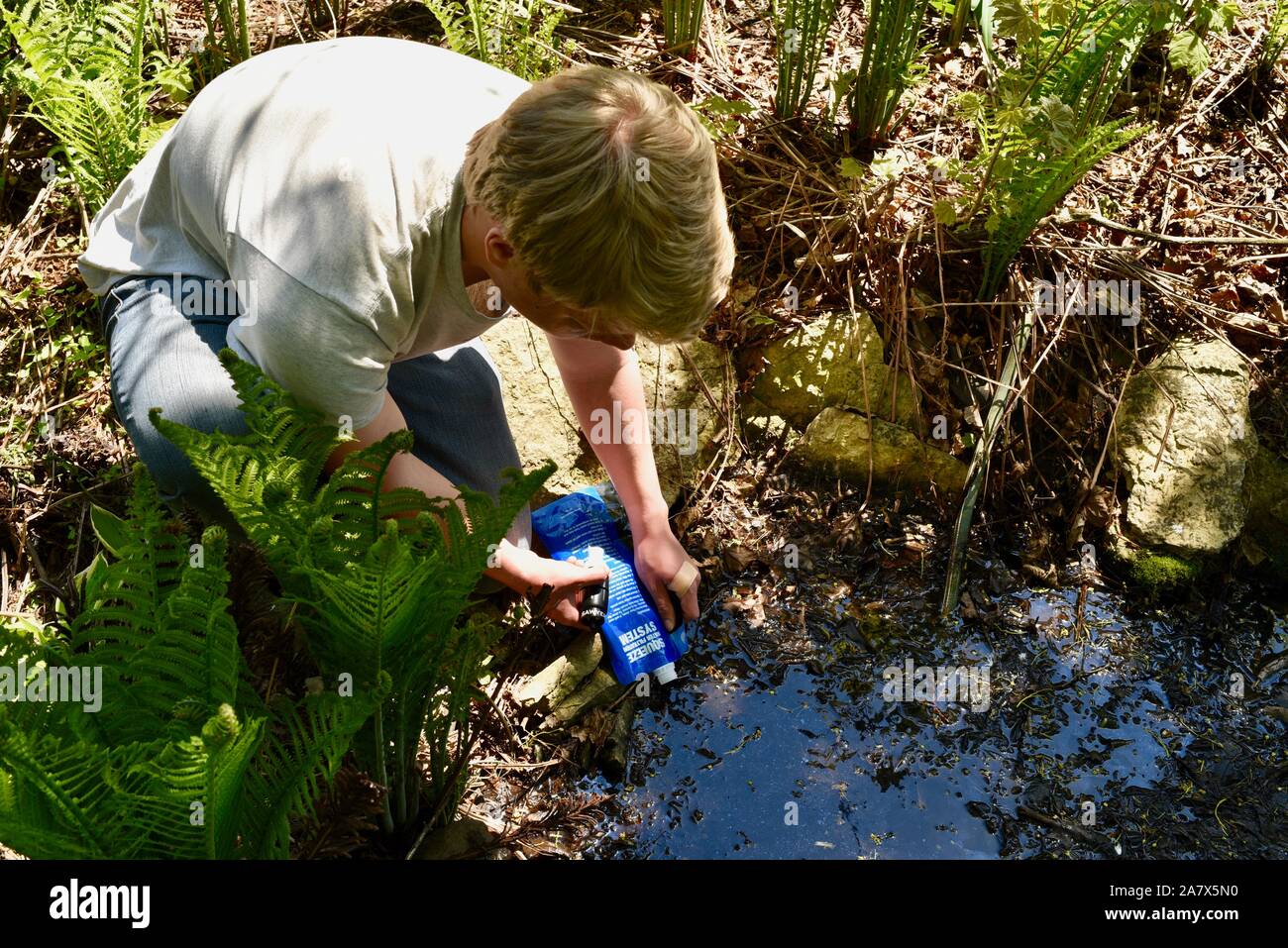 Junger Mann mit Sawyer Squeeze Wasser-filtersystem Wasser für sicheres Trinkwasser zu reinigen, Trinkwasser, von Teich, browntown Wisconsin, USA. Stockfoto