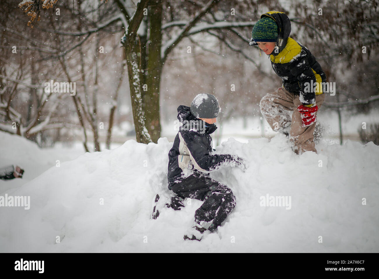 Zwei Jungen spielen auf Haufen Schnee nach starker Schneefall in der Stadt. Kinder, die auf einem Spaziergang im Park im Winter. Aktiv gesund Lifestyle. Stockfoto