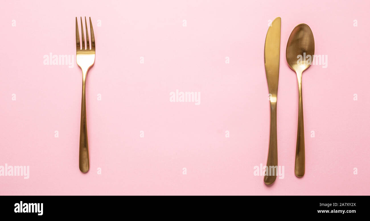 Gold und Pink luxus Tabelle einstellen. Golden Besteck gegen rosa Hintergrund gesetzt. Ansicht von oben, kopieren Raum Stockfoto