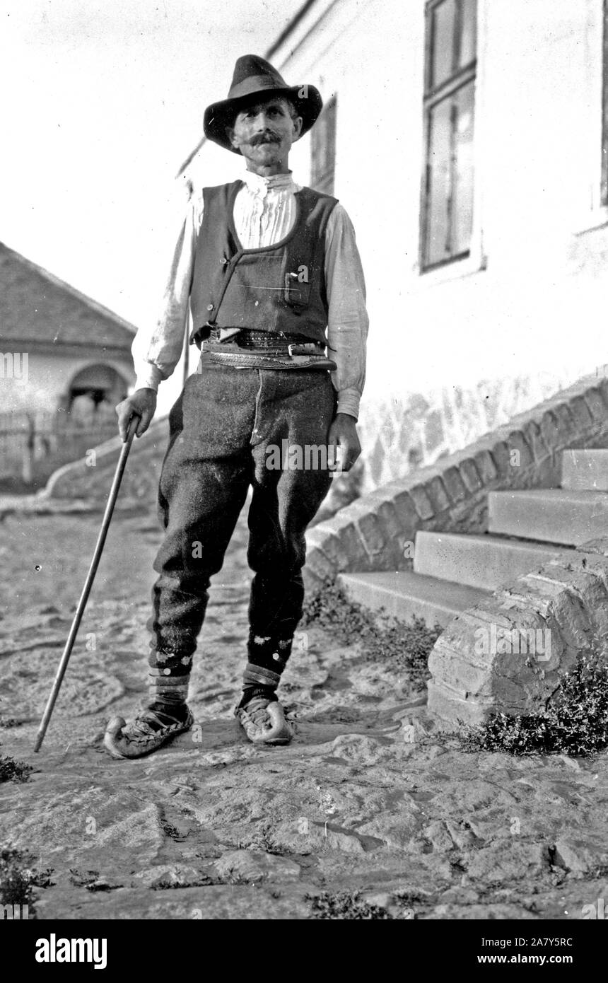 Serbische Mann mit Hut, Hemd, Hose, Gürtel und spitzen Schuhe mit Zuckerrohr stehen außerhalb der Gebäude in Jugoslawien c 1918-1924 Stockfoto