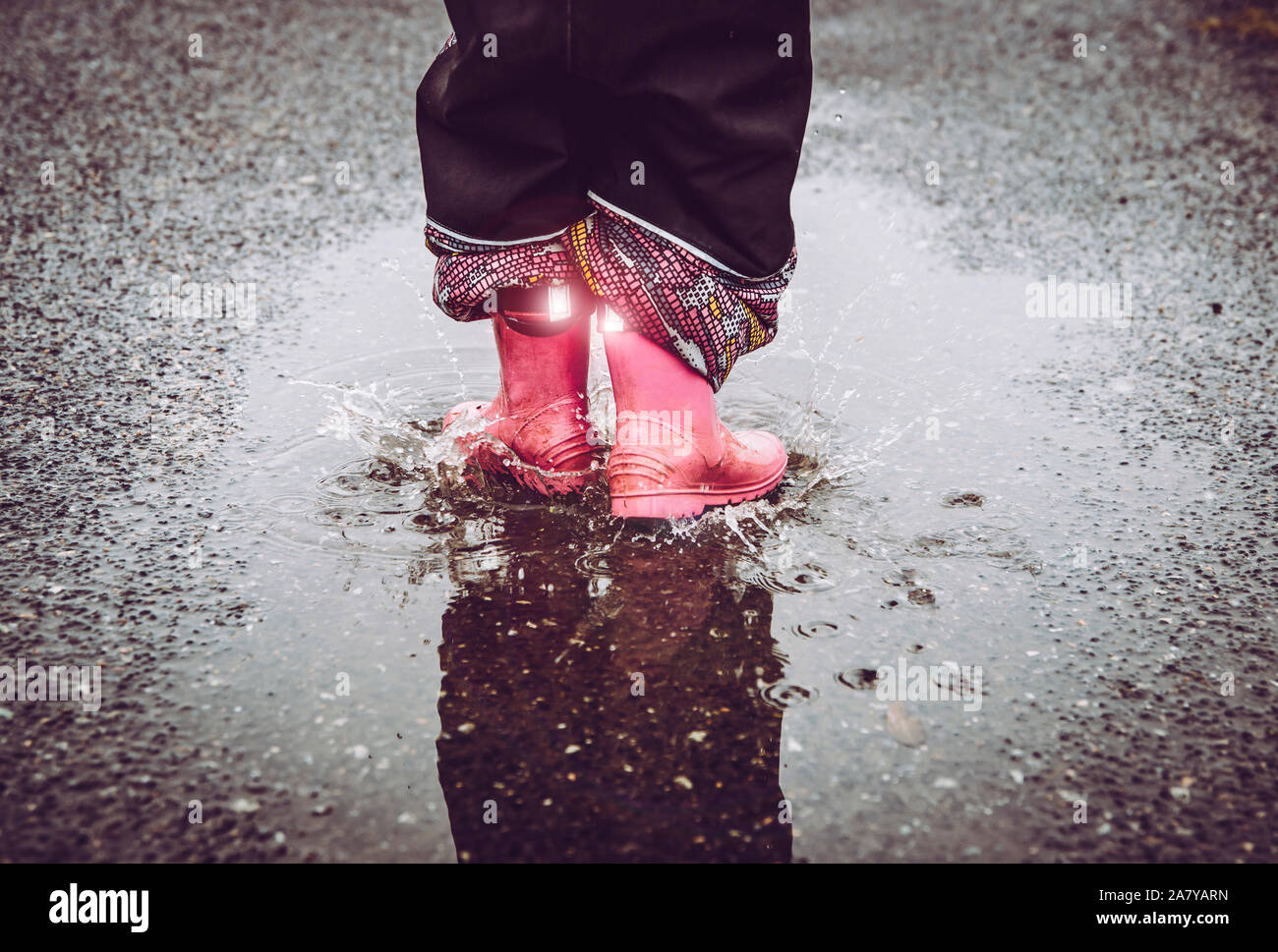 Mädchen Spaß, im Wasser Pfütze auf nasser Straße springen, das Tragen von regen Stiefel mit Reflektierende Details Stoff Streifen scheint. Hohe Sichtbarkeit und Sicherheit i Stockfoto