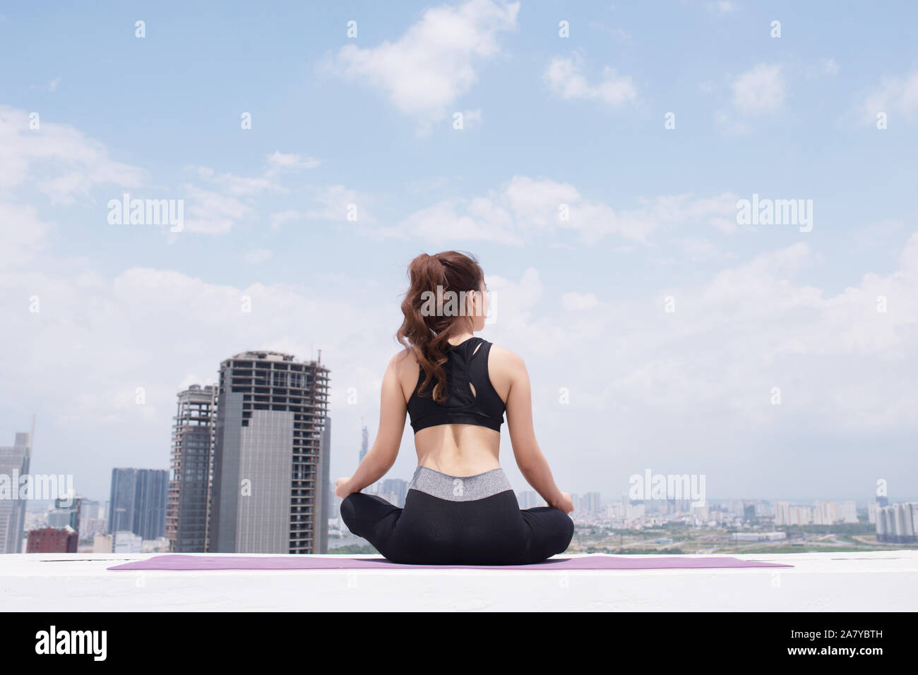Ruhige junge Sportlerin im aktiven tragen sitzen in Pose während Yoga Ausbildung auf Gebäude auf dem Dach Stockfoto