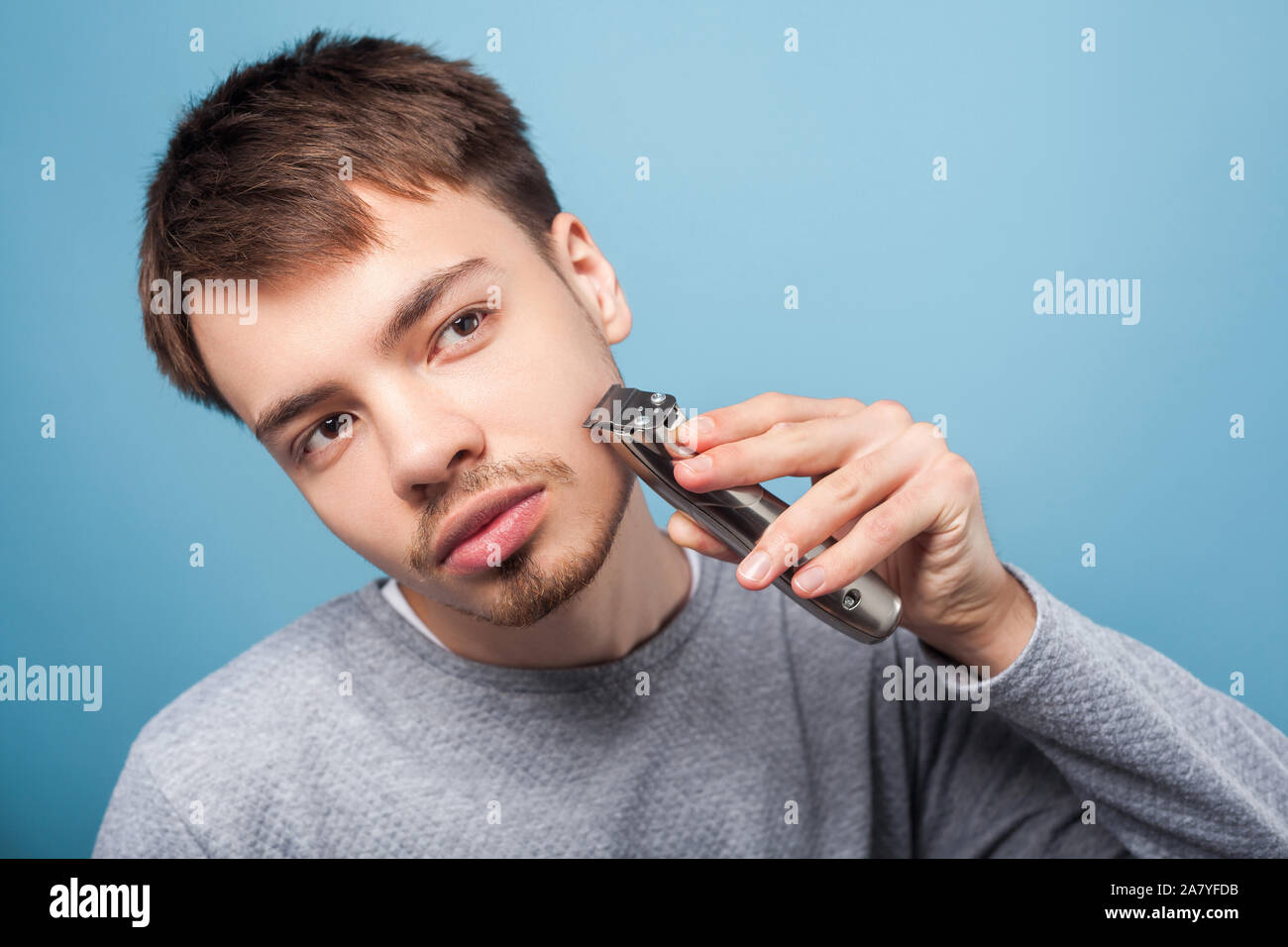 Rasieren Routine. Porträt der jungen Hübschen brünetten Mann in lässiger Pullover Rasieren mit dem Trimmer suchen Wie im Spiegel seinen Bart zu gestalten, attenti Stockfoto