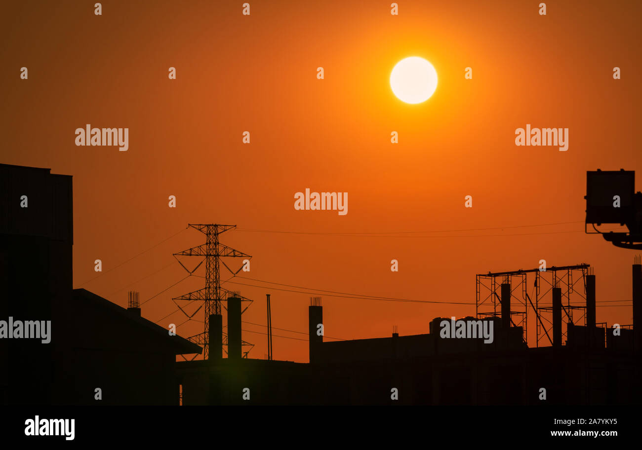 Silhouette Baustelle mit orange Sonnenuntergang Himmel Hintergrund. Hohe Spannung der elektrischen Tower. Schöne große Sonne bei Sonnenuntergang in der Stadt. Dramatischer Himmel Stockfoto