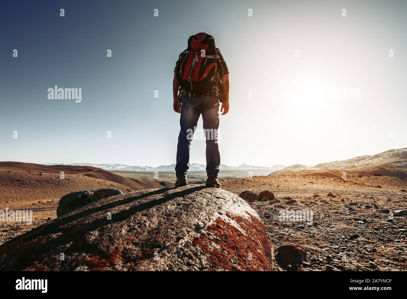Wanderer mit Rucksack steht auf Big Rock gegen Berge und den Sonnenuntergang Stockfoto