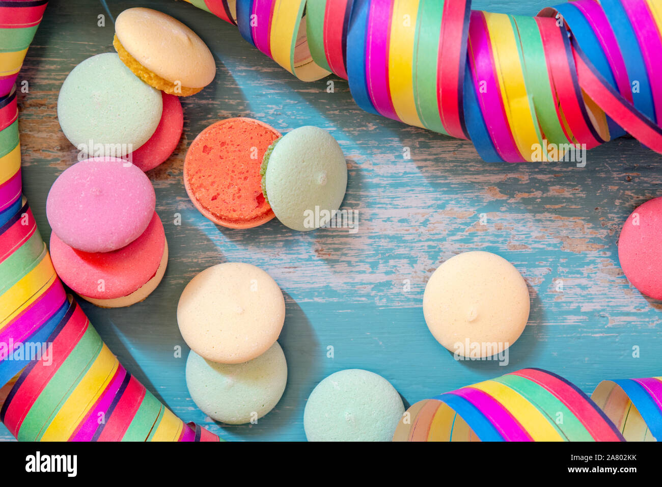 Macarons oder Kekse mit bunten Papier Streamer auf blauem Hintergrund, Geburtstag oder Karneval Thema Stockfoto