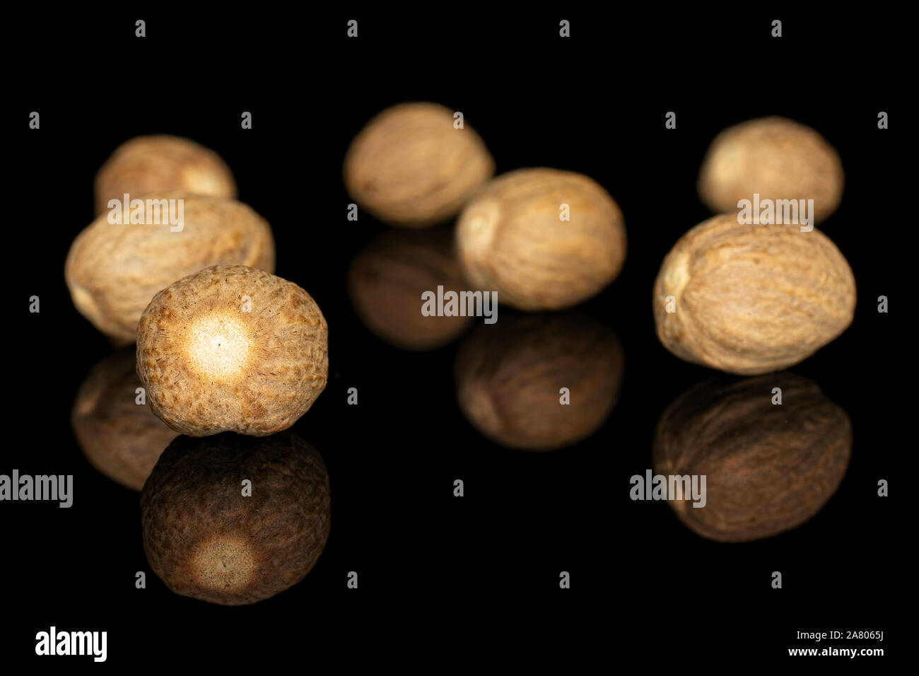 Gruppe von Sieben ganze Trockene braun Muskatnuss auf schwarz Glas isoliert Stockfoto