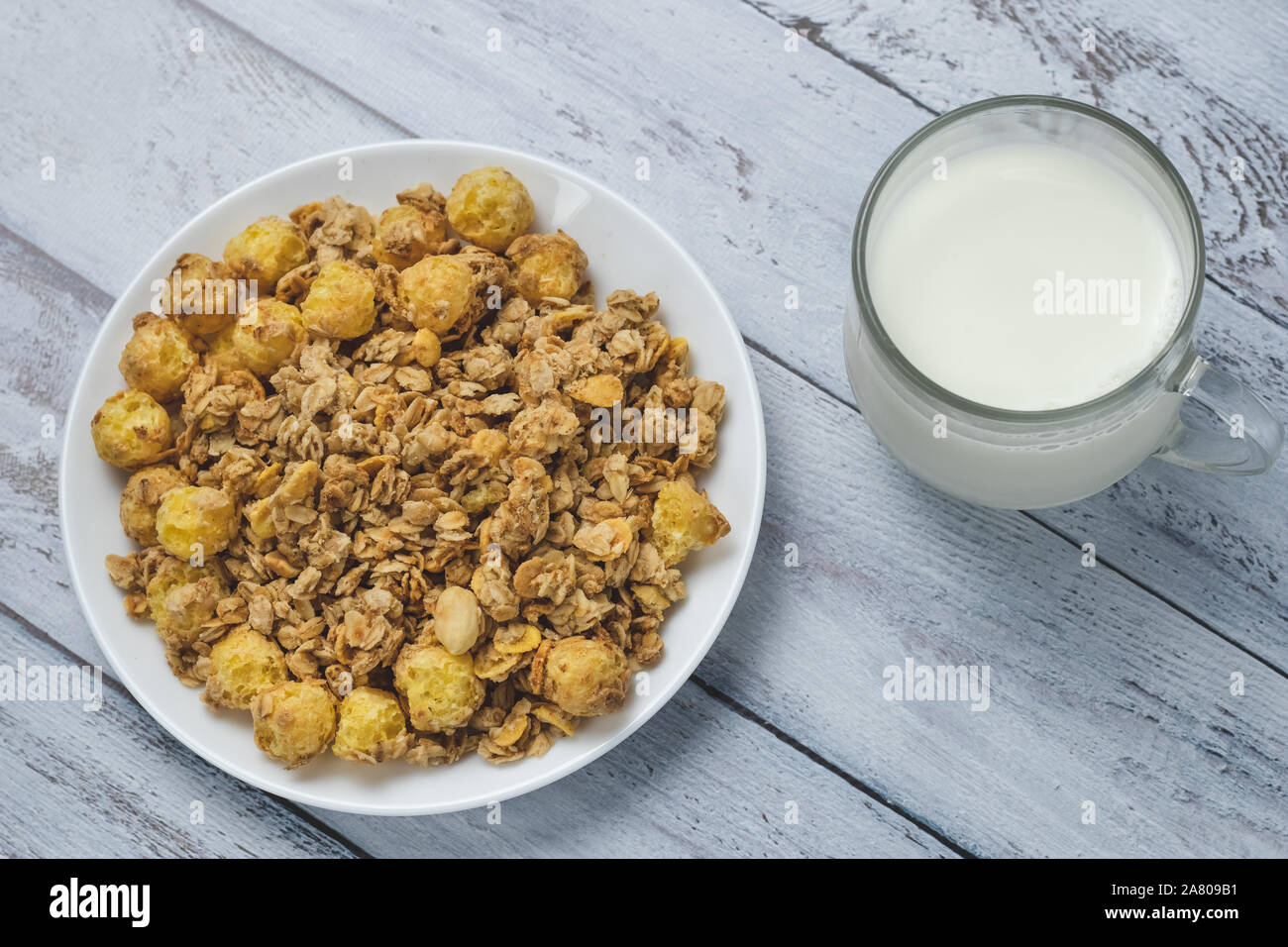 Weiße Platte von Müsli mit Glas Milch auf grau Holzbretter. Eine Mischung von Getreide getrocknet und Muttern mit Milch zum Frühstück. Glas Tasse Milch mit Ro Stockfoto