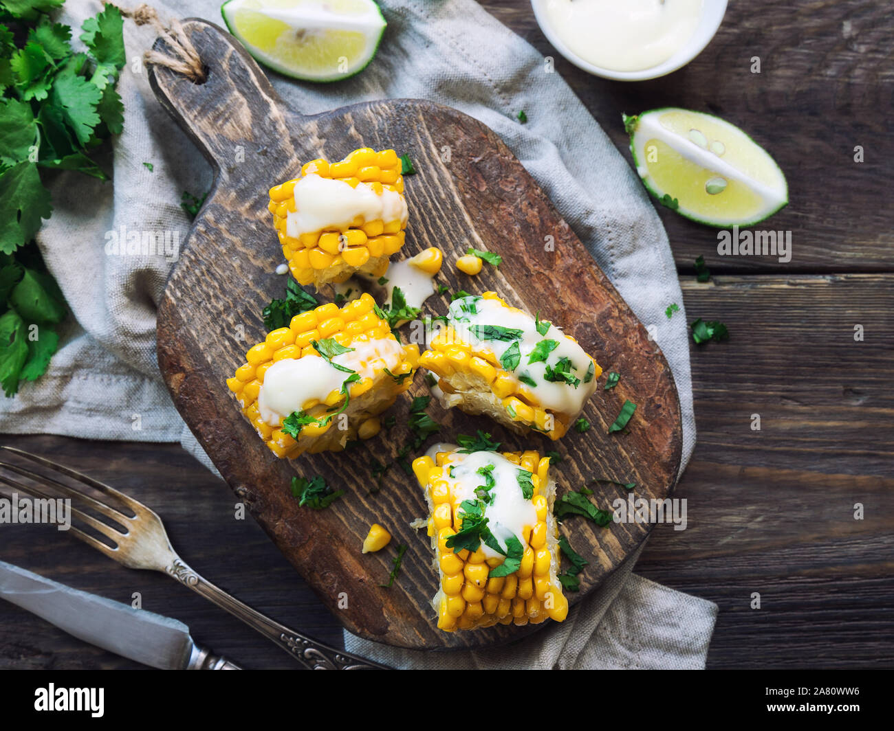 Frisch gebackene Maiskolben mit Aioli Sauce und Koriander auf rustikalen Holzmöbeln Hintergrund. Gesunde vegetarische Nahrung. Ansicht von oben. Stockfoto