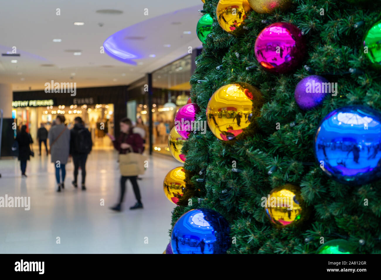 Weihnachtskäufer vorbei gehen. einen Weihnachtsbaum mit leuchtenden Kugeln in einem Einkaufszentrum eingerichtet Stockfoto