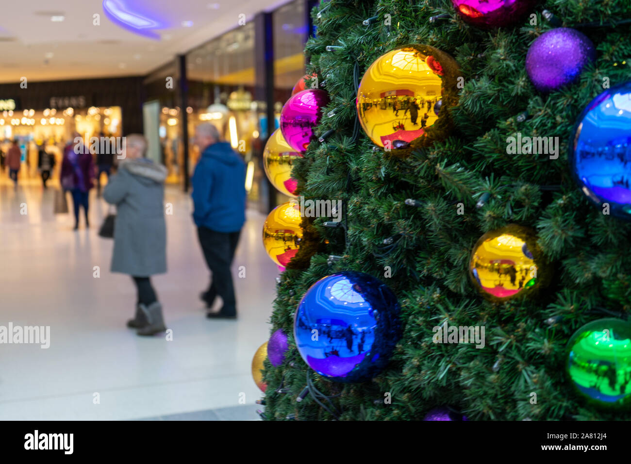 Weihnachtskäufer vorbei gehen. einen Weihnachtsbaum mit leuchtenden Kugeln in einem Einkaufszentrum eingerichtet Stockfoto