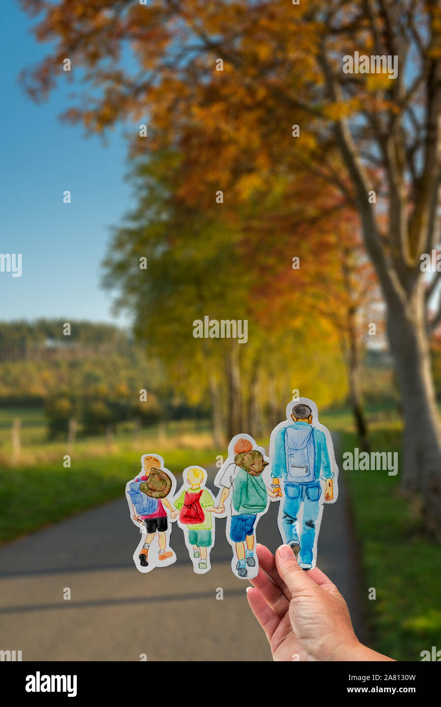 Eine gepflasterte Straße führt durch sonnige Herbst Landschaft mit orange verlässt. Hand hält Zeichnung mit Wandern Familie mit Rucksäcken. Stockfoto