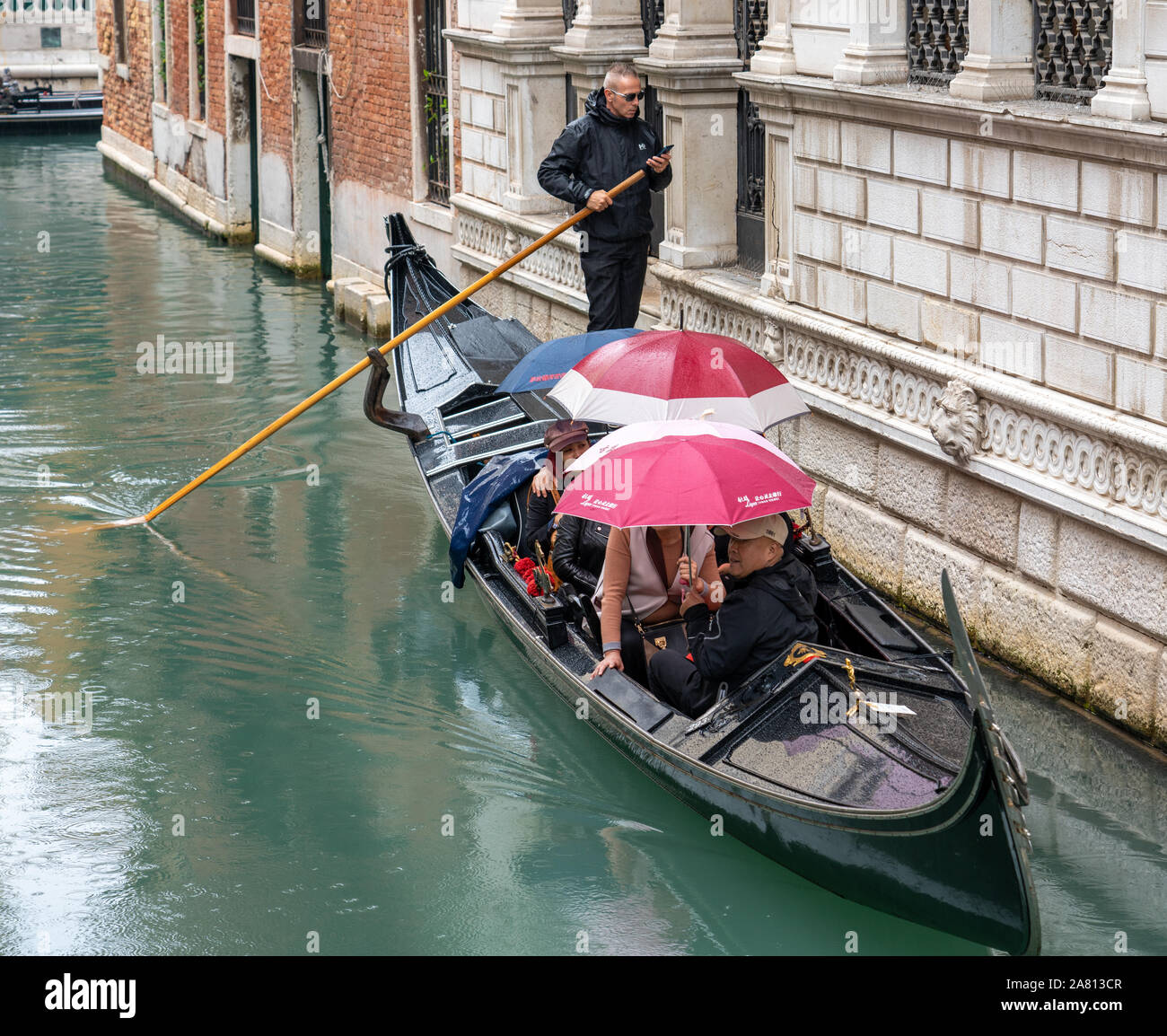Ein gondoliere auf sein Handy während der Überführung von Touristen um einen regnerischen Venedig Italien Stockfoto