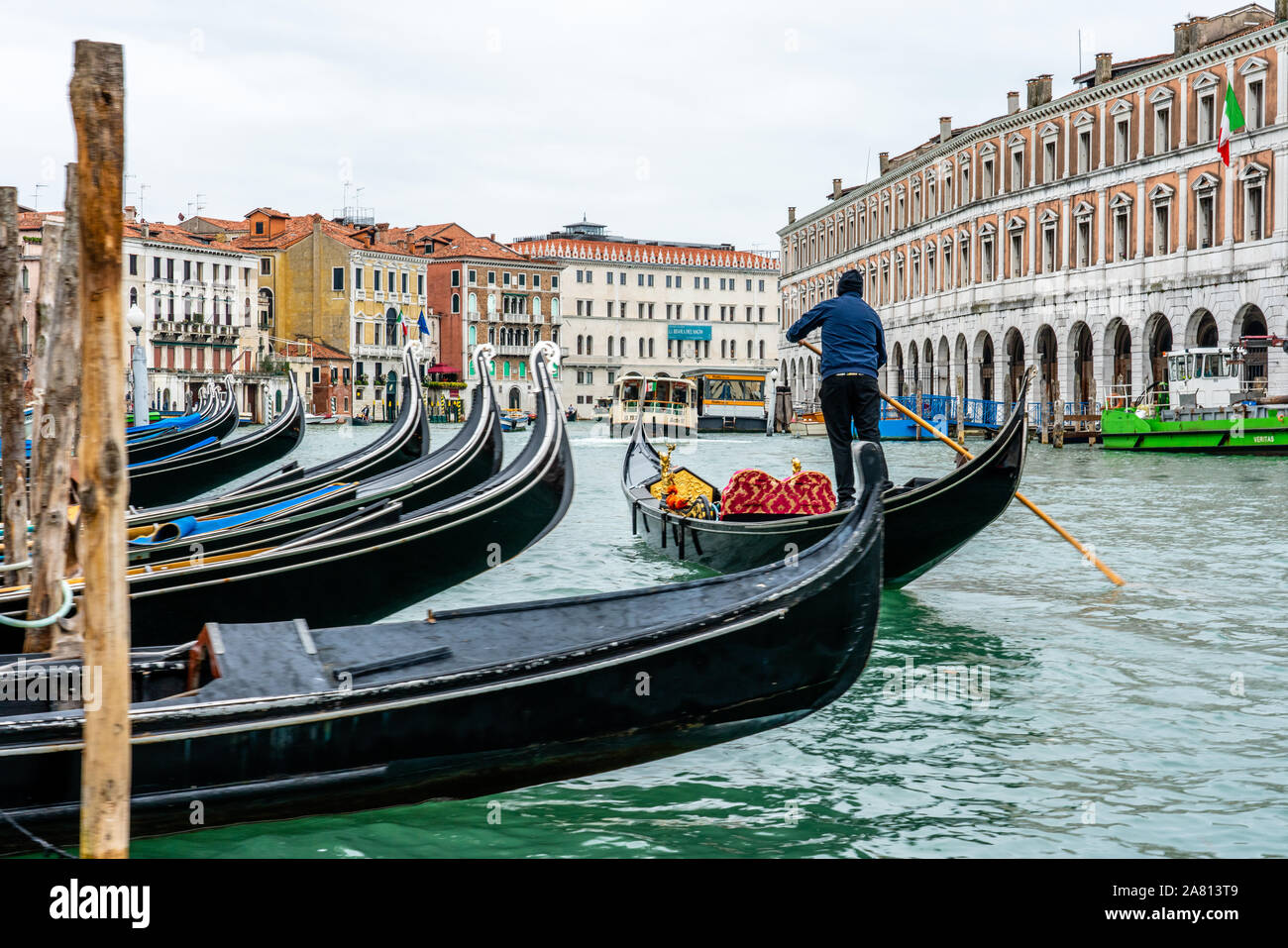 Ein gondoliere Lenkung seine Gondel Vergangenheit eine Linie der angelegten Boote am Grand Canal in Venedig Italien Stockfoto