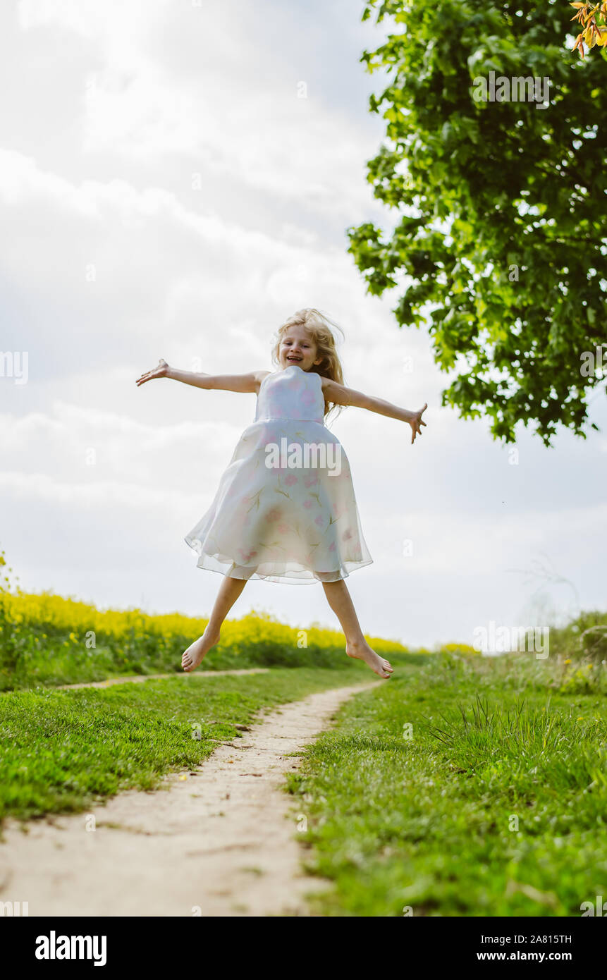 Springen Abbildung von kleinen Mädchen in weißem Kleid in grün frühling landschaft Stockfoto