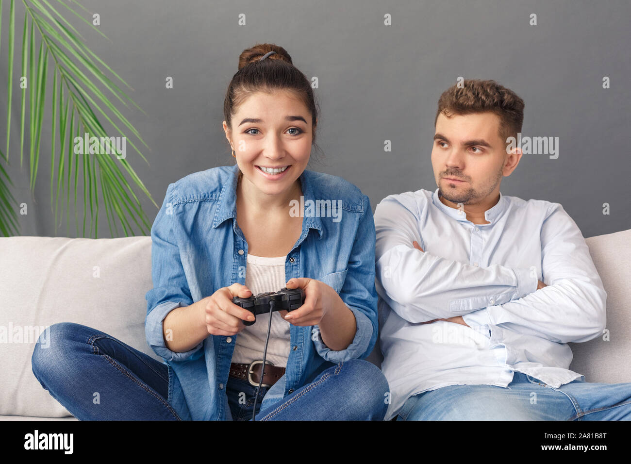 Relationnship Konzept. Junges Paar sucht Mann wütend auf Frau spielen video game konzentriert Sitzen auf einem Sofa studio isoliert auf Grau Stockfoto