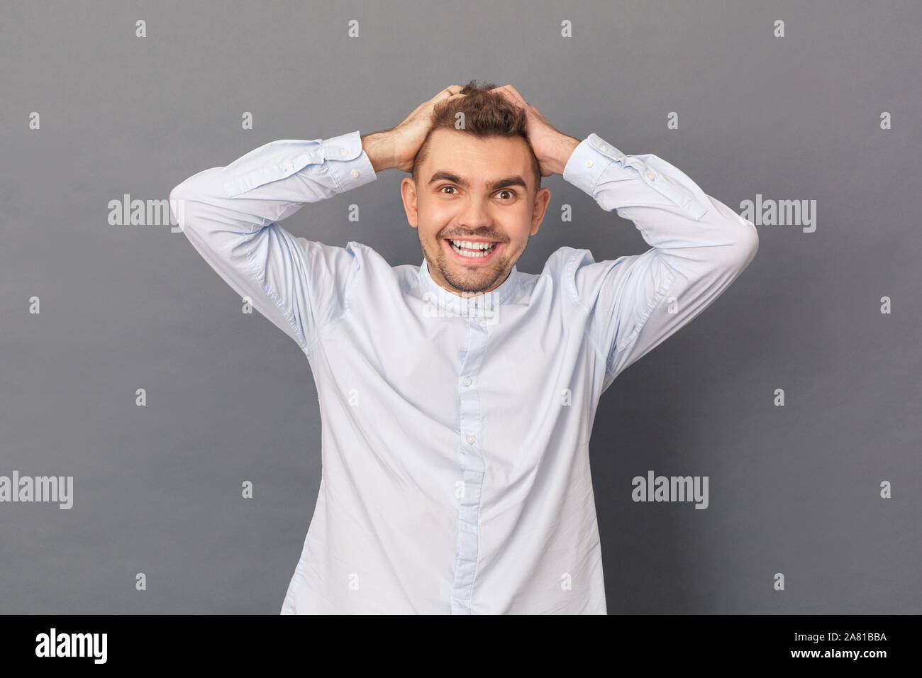 Freestyle. Junger Mann Studio stehen auf Grau holding Kopf isoliert Lachen heiter Stockfoto