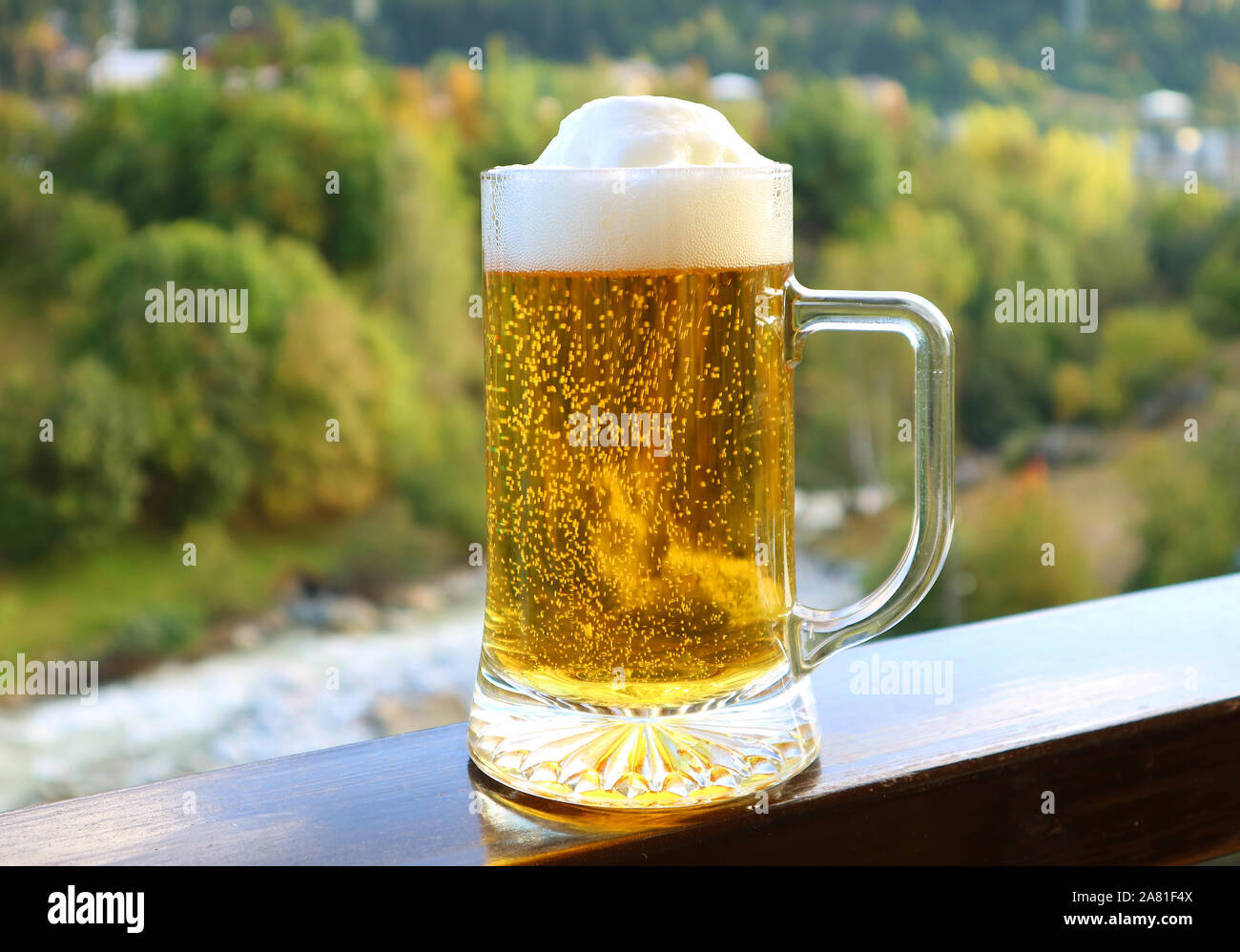 Ein Pint Bier auf dem Balkon Geländer mit verschwommenen Blick auf den Wald Stockfoto