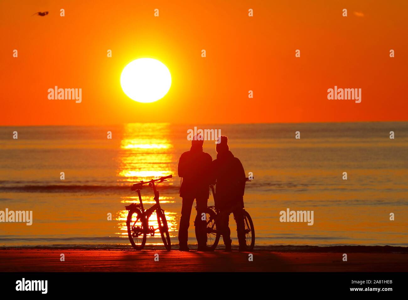 Paare mit Fahrrädern am Strand den Sonnenuntergang beobachten, Nordsee, St. Peter-Ording, Nordseeküste, Nationalpark Schleswig-Holsteinisches Wattenmeer Stockfoto