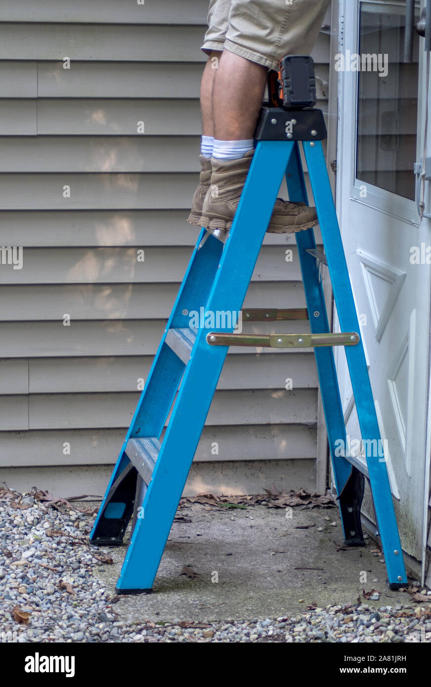 Ein Arbeiter steht auf einer Leiter, als er draussen auf der Außenseite eines Hauses funktioniert Stockfoto