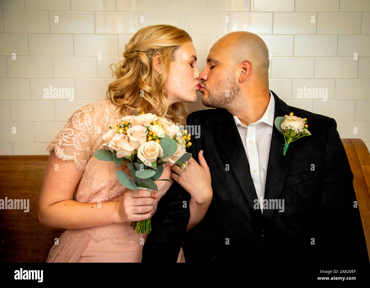 Nahaufnahme von Braut und Bräutigam in Vintage Kleidung sitzen und berühren und Küssen mit Braut holding Blumenstrauß warten zu heiraten Stockfoto