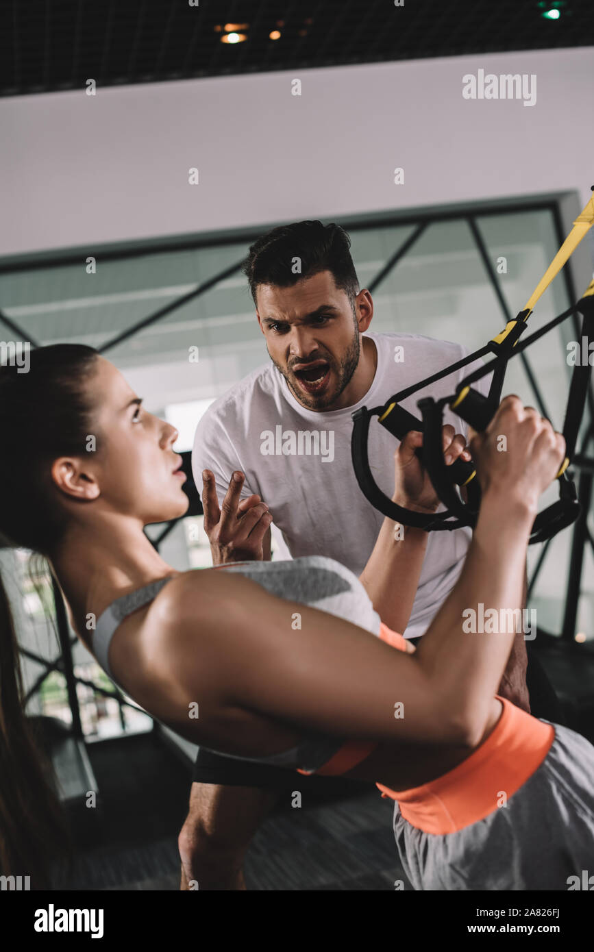 Aufgeregt trainer Schreien während motivieren junge Sportlerin das Hochziehen Suspension Trainer Stockfoto