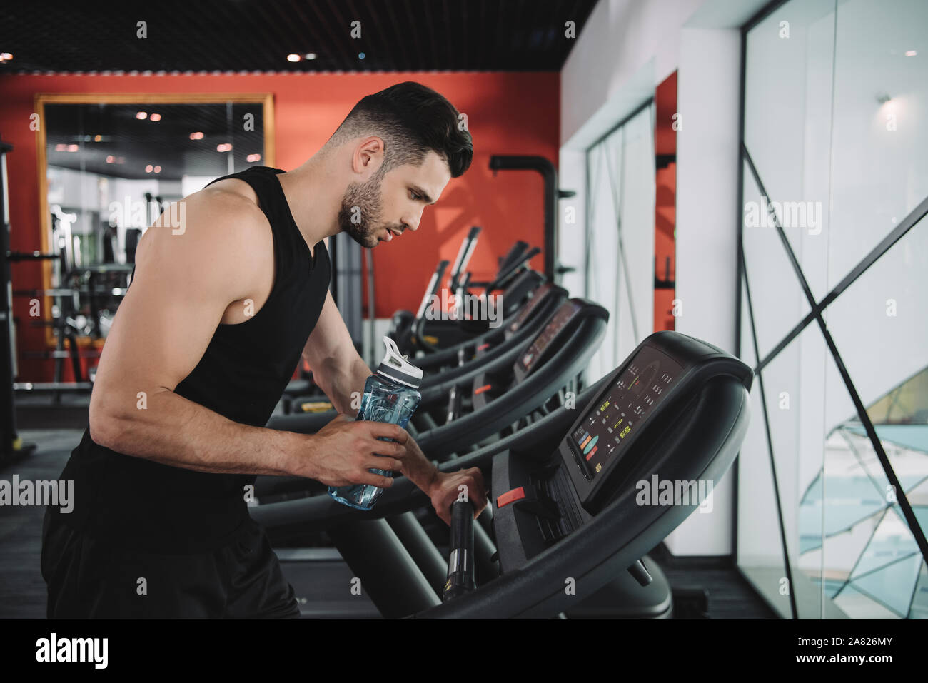 Schöne, junge Sportler suchen, die auf dem Bedienfeld des Laufband halten Sport Flasche Stockfoto