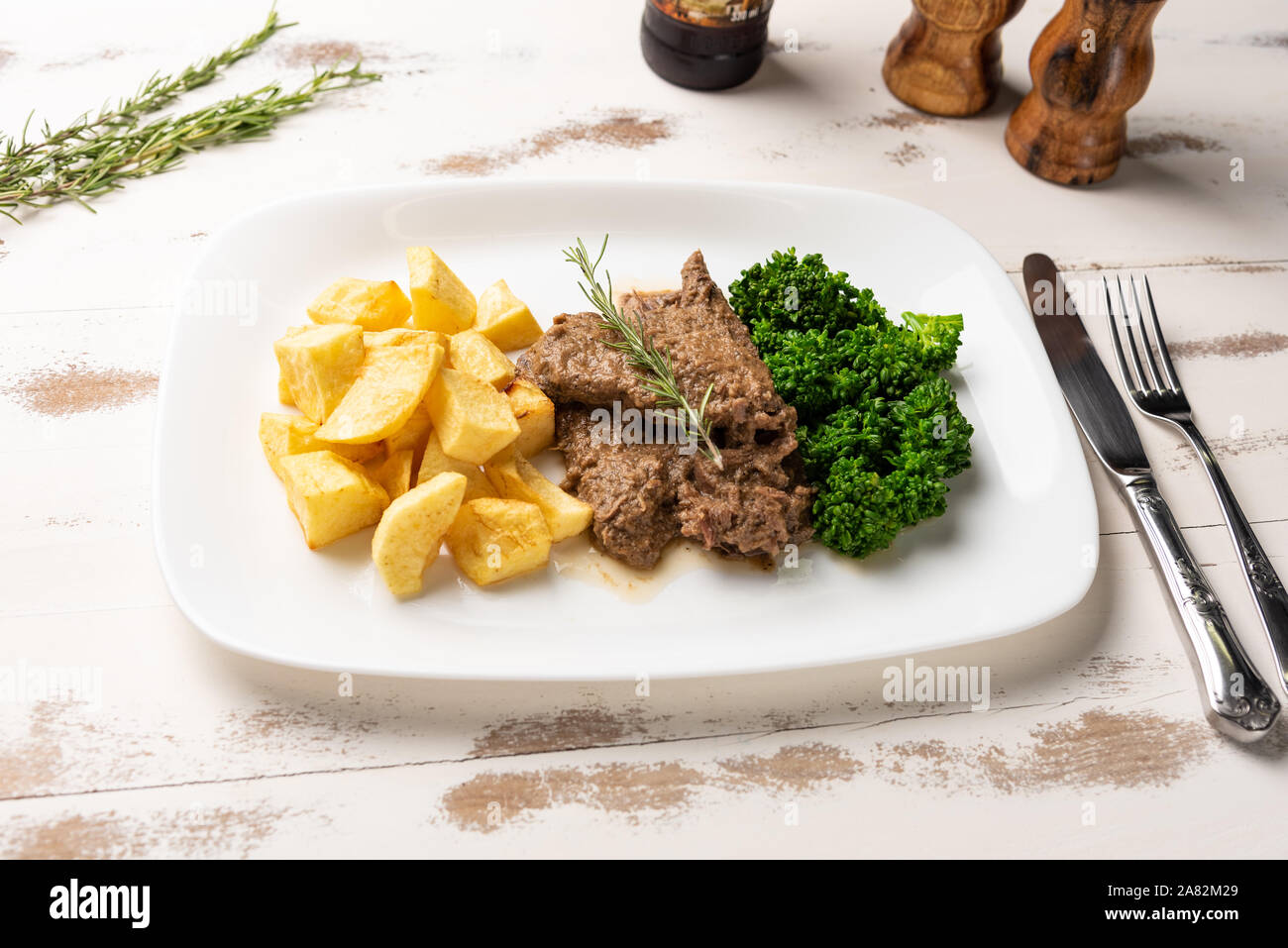 Rinderragout mit rustikalen Kartoffeln und Brokkoli in einer weißen Platte auf weiße Holztisch Hintergrund, weiches Licht Stockfoto