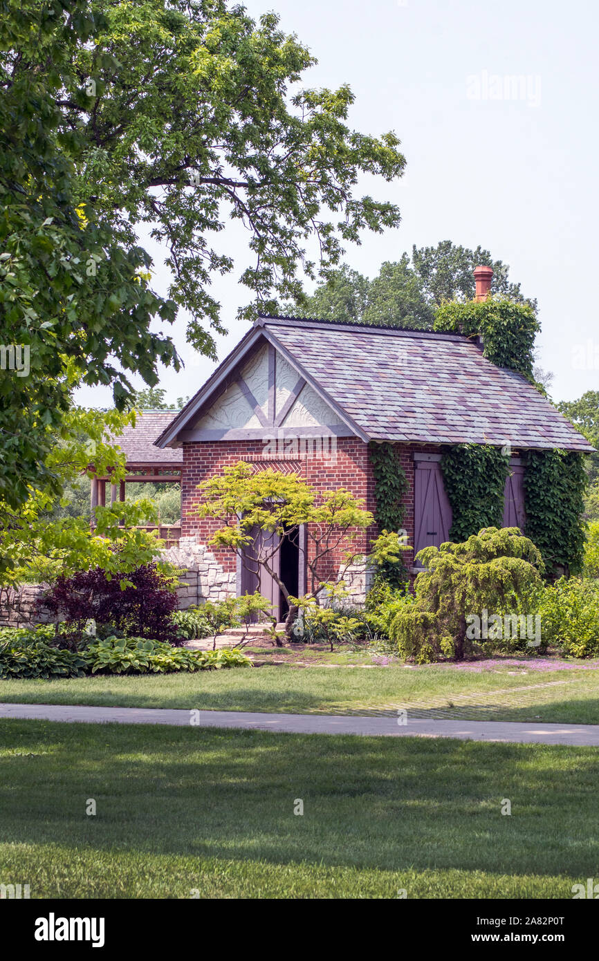 Eine kleine Cottage liegt in einem schönen Garten, mit grünen Bäumen und Pflanzen und Klettern Efeu an den Wänden Stockfoto