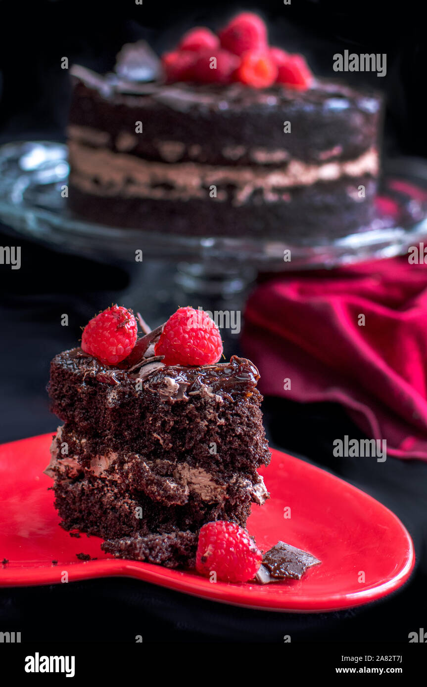 Köstliches Stück Schokoladenkuchen ruht auf einem leuchtend roten Platte und ist mit frischen Himbeeren garniert Stockfoto