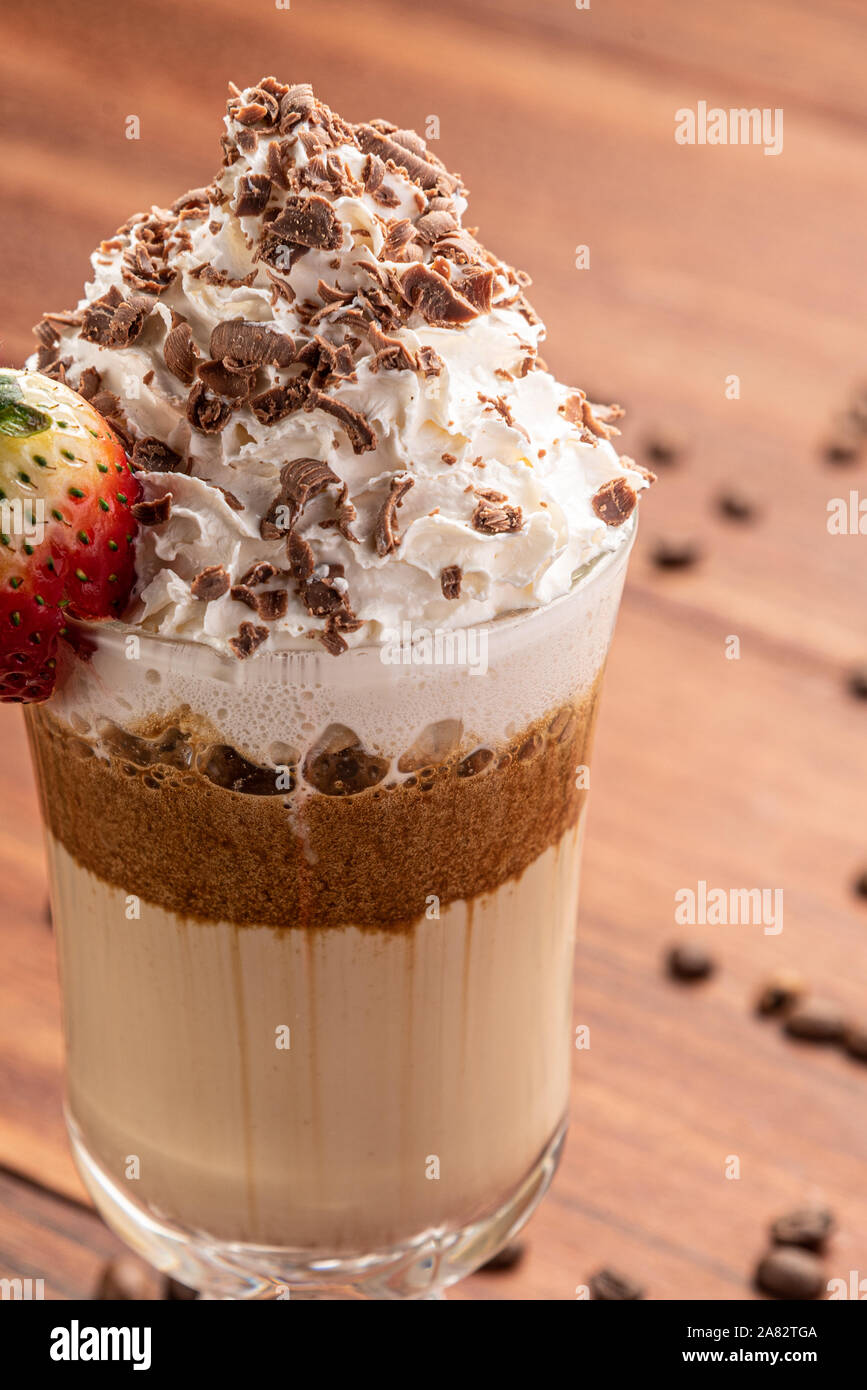 Kalter Kaffee trinken Frappe (frappuccino), mit Sahne und Schokolade Schreibfedern, mit Körnern von Kaffee auf Holz- Hintergrund Stockfoto