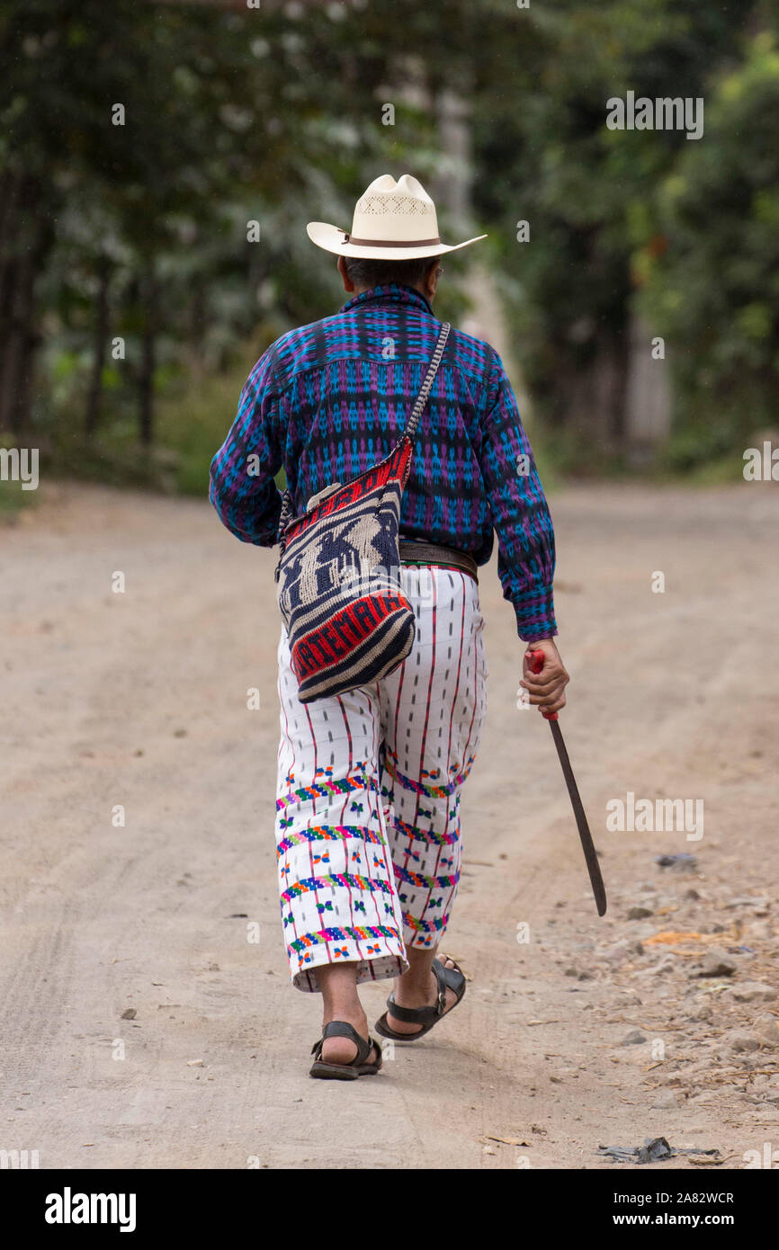 Eine ältere Maya Bauer das Tragen der Tracht von San Pedro La Laguna, Guatemala, zu seinem kleinen Bauernhof auf einer Schotterstraße, Durchführung einer Machete Stockfoto