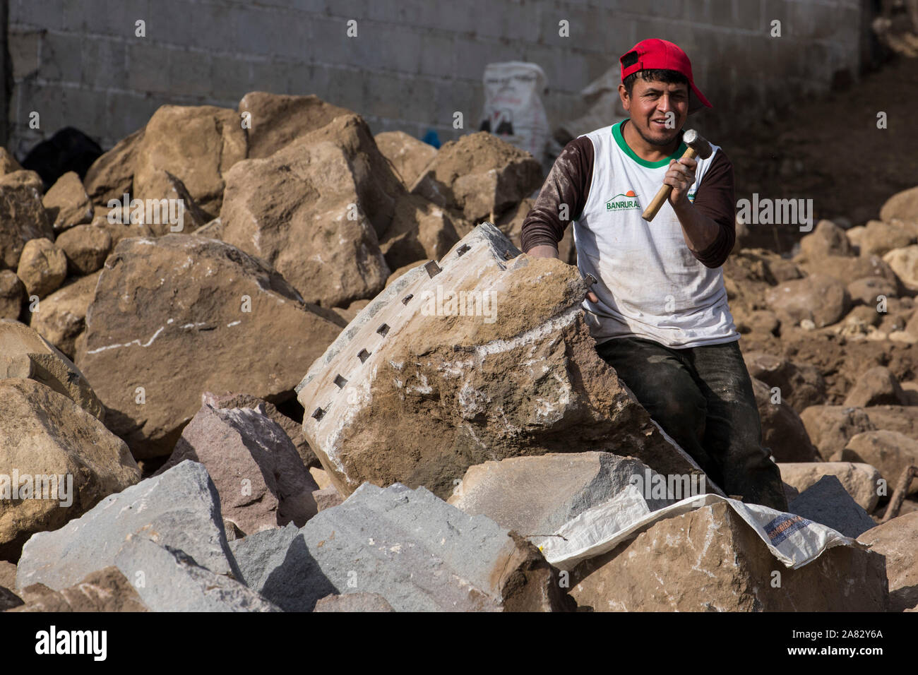 Ein junger Mann spaltet große Felsen von Hand mit einem kleinen Sledgehammer und Stahl Keile in San Pedro La Laguna, Guatemala. Stockfoto
