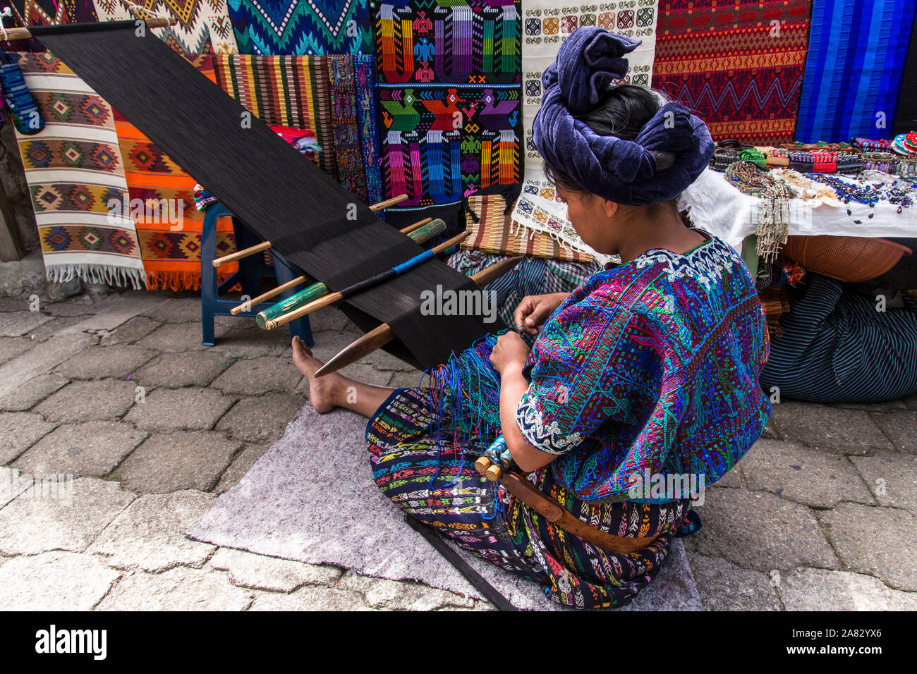 Ein Maya Frau in traditioneller Kleidung auf dem Boden sitzend und Weberei auf einem backstrap in Santa Catarina Palopo, Guatemala Webstuhl. Fertige weavings hängen Stockfoto