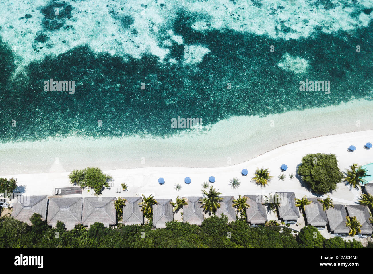 Luftaufnahme von tropischen weißen Strand mit blauen Schirme, Coral Reef und Palmen. Abstrakte drone Schuß von oben. Reisen und Urlaub Konzept. Stockfoto
