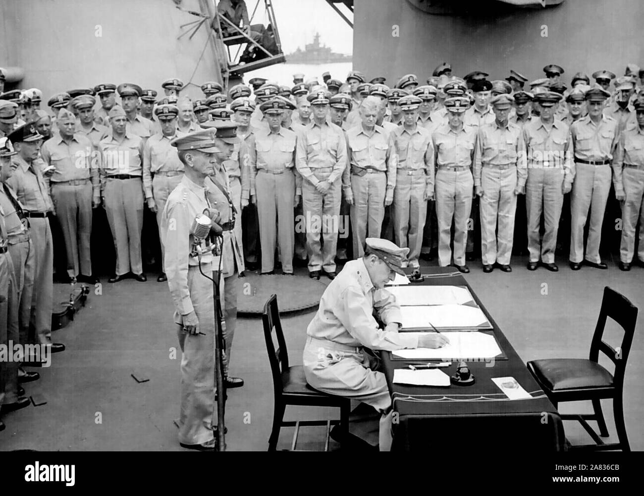 General Douglas MacArthur Zeichen als Oberster Alliierter Befehlshaber während der formalen Übergabe Zeremonien auf der USS Missouri in der Bucht von Tokio. Hinter General MacArthur sind Generalleutnant Jonathan Wainwright und Generalleutnant A.E. Percival. September 2, 1945 Stockfoto