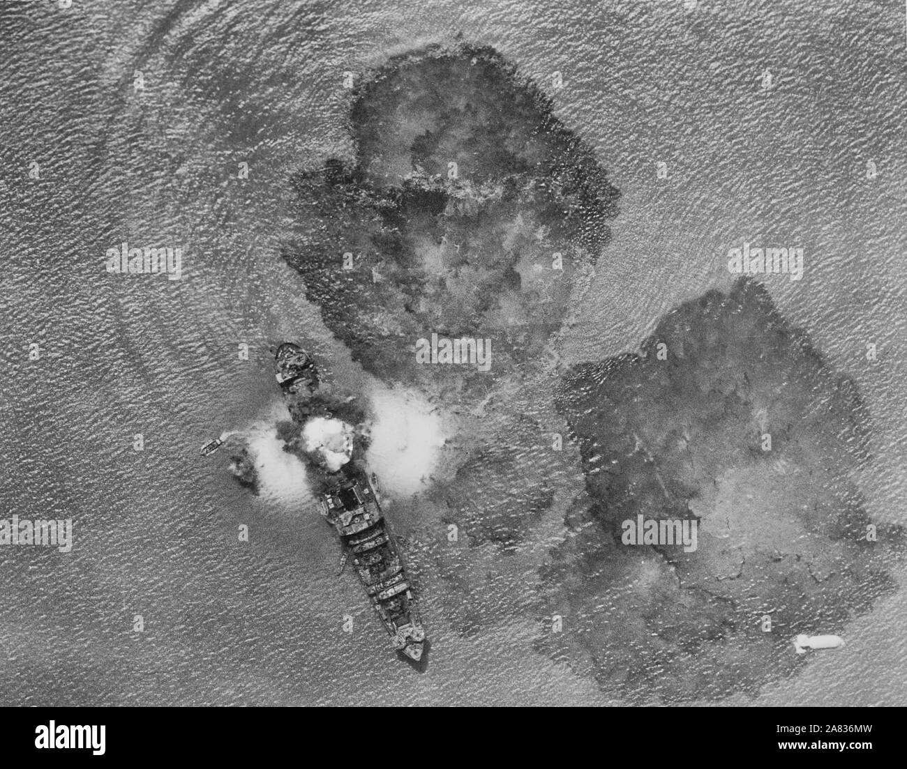 Ein 7.000 Tonnen japanisches Handelsschiff nach einem direkten Treffer durch Indien Air Task forces in der Nähe von Rangun, Indien. Eine Bombe fällt im unteren rechten Teil des Bildes und kleinen Booten versuchen, die Mitglieder der Besatzung vom sinkenden Schiff zu tragen. Die Gewässer sind mit Öl bedeckt. Ca. 1943 Stockfoto