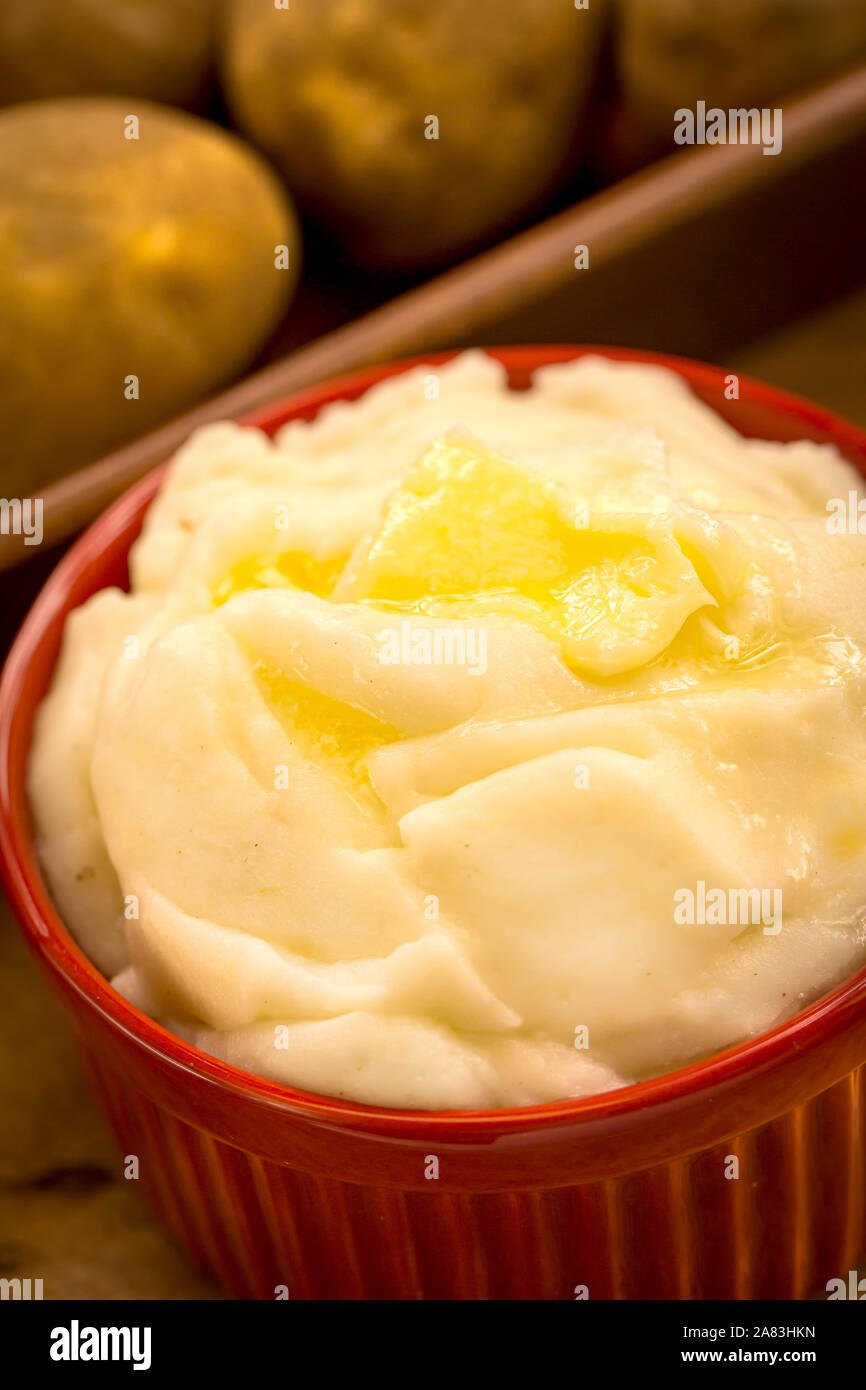 Kartoffelpüree in rotem Ramekin mit Butter mit Kartoffeln im Hintergrund Stockfoto