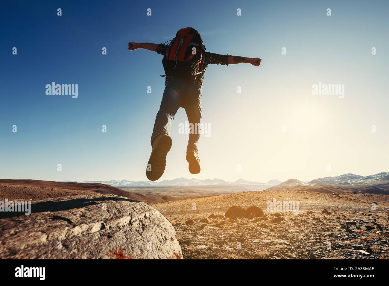 Wanderer mit Rucksack springt von Big Rock gegen Berge und den Sonnenuntergang Stockfoto