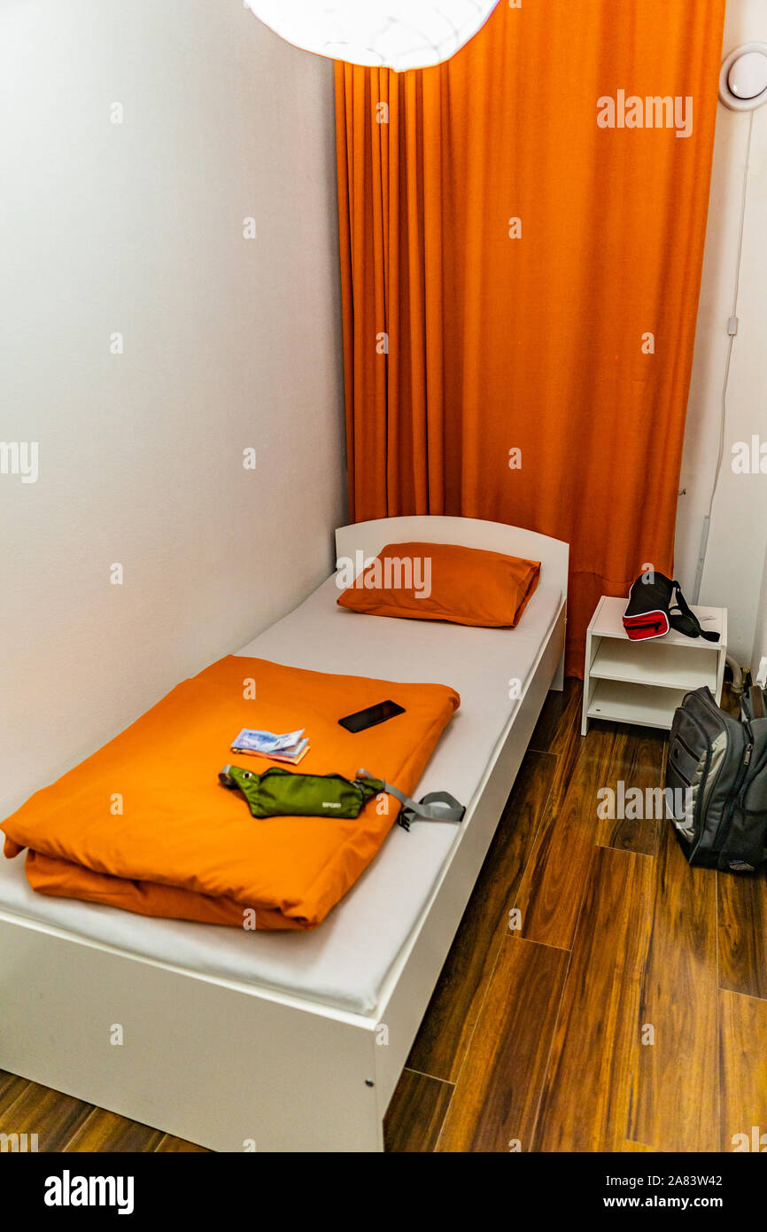 Hostel einfach Einzelzimmer mit orangefarbenen Vorhang Bettwäsche und bescheidenen Schaltkasten Stockfoto