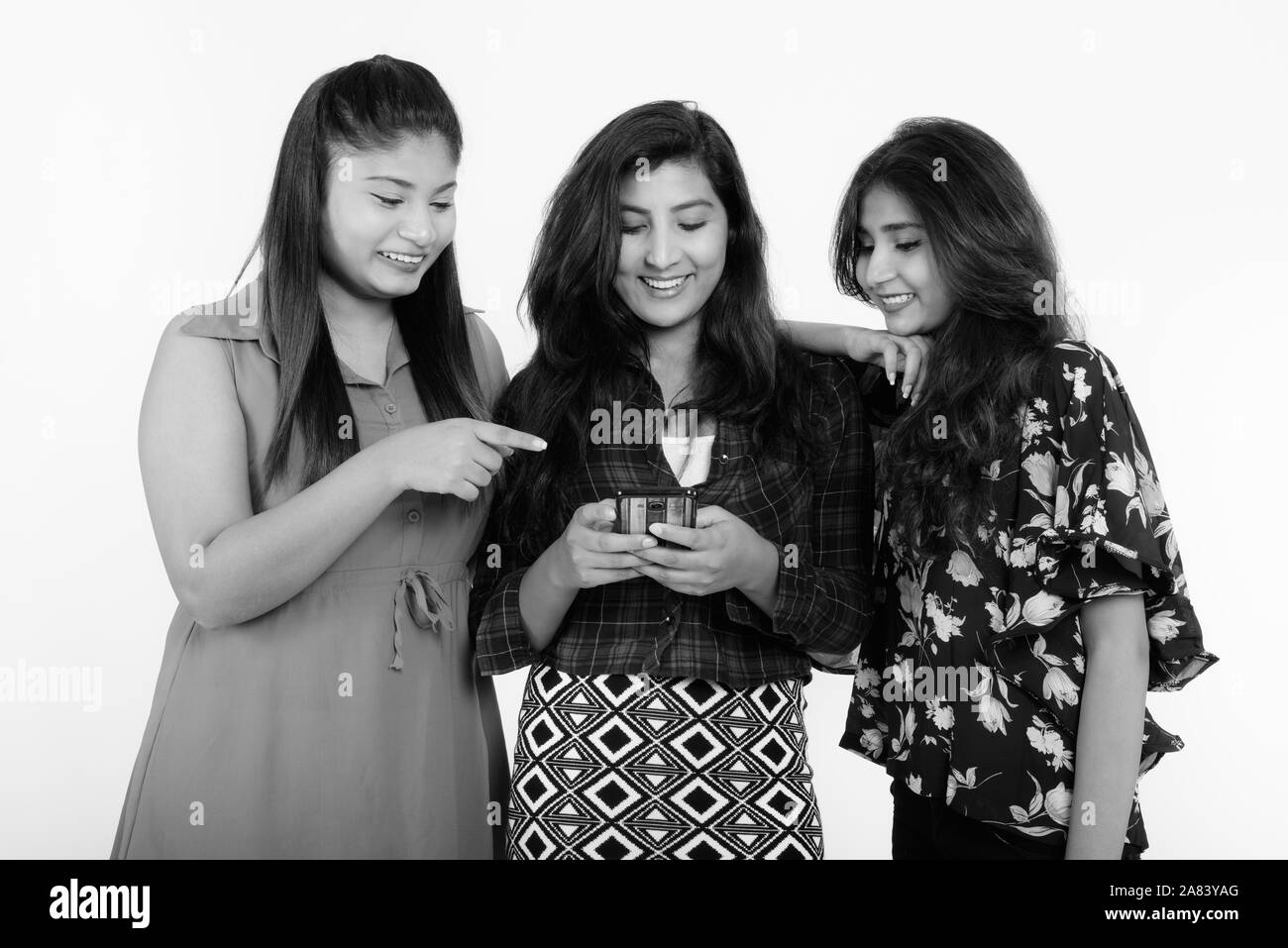 Studio shot von drei glückliche junge persische Frau Freunde lächelnd, während Sie ein Handy zusammen Stockfoto