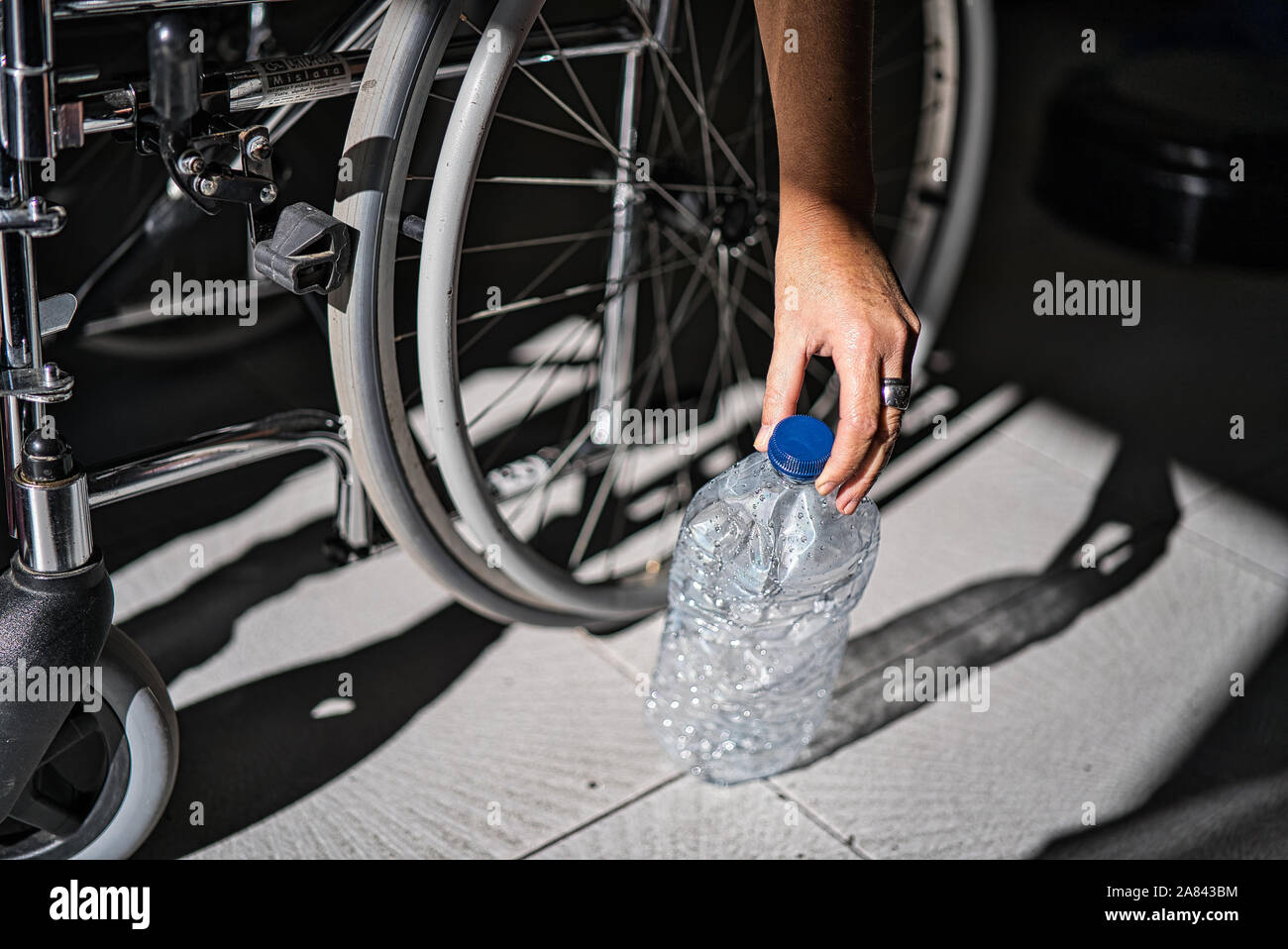 Rollstuhl behinderte Person Aufnehmen einer transparenten Kunststoff Flasche geworfen und auf dem Boden aufgegeben es in den Abfall Recycling Container zu werfen Stockfoto