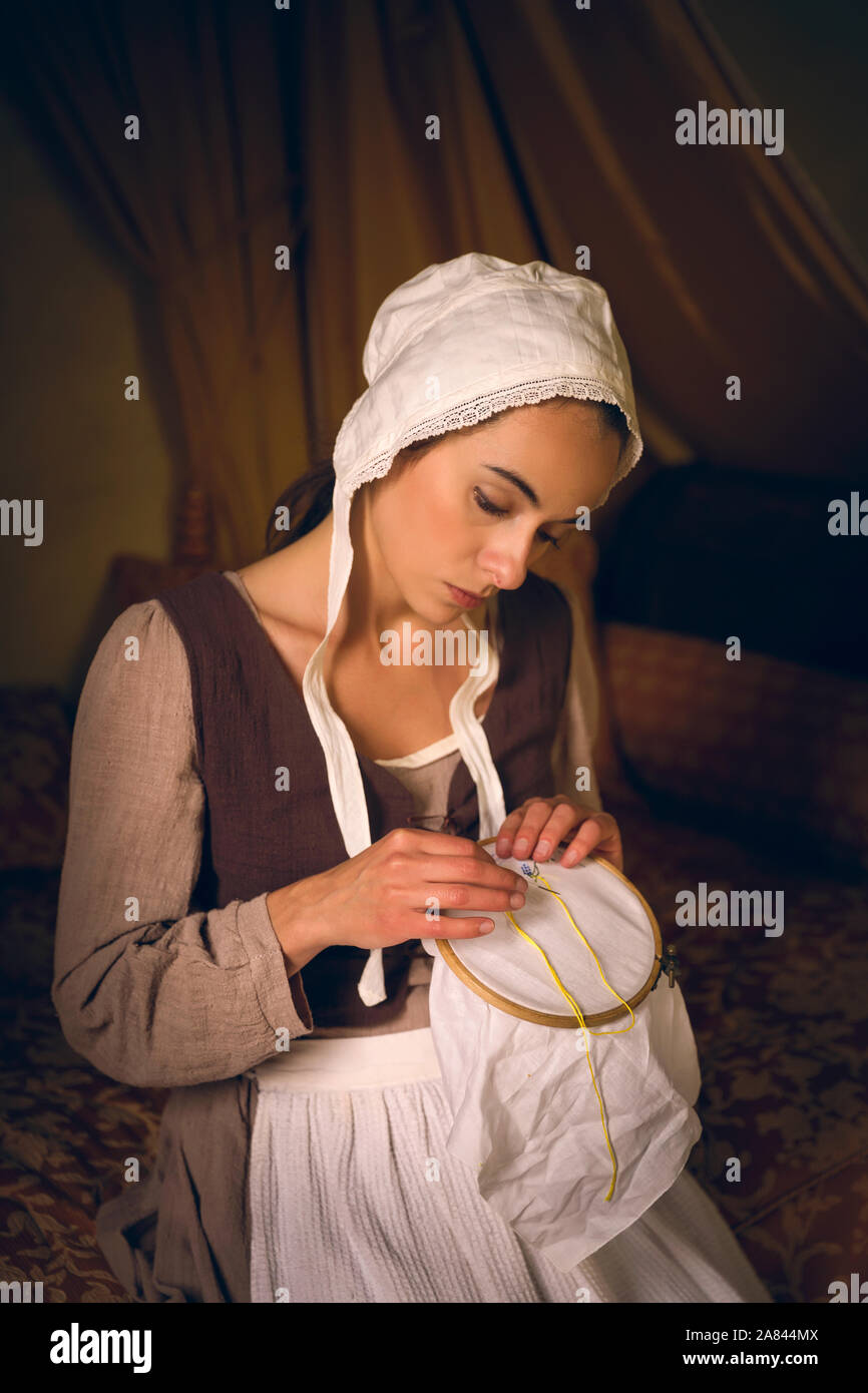 Vermeer Stil Porträt einer jungen Magd in Renaissance Kostüm sitzen auf einem antiken Bett mit ihrem Stickereien Stockfoto
