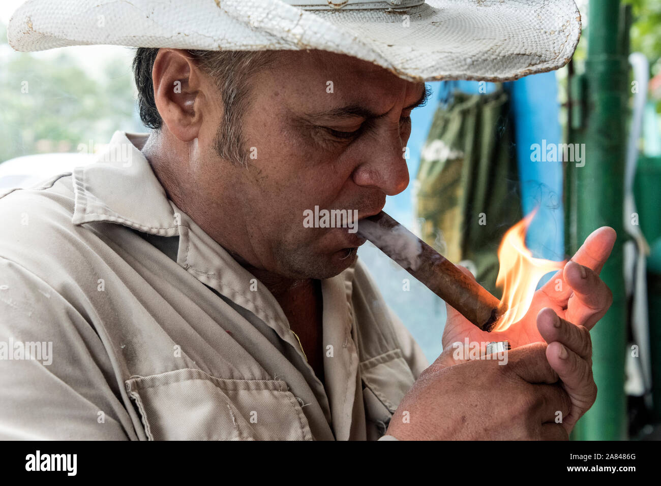 Ein kubanischer Bauer/Besitzer mit traditionellem kubanischem Hut zündet seine handgerollte Zigarre mit einem Feuerzeug an, im Valle de Vinales, Provinz Pinar del Río, A Stockfoto