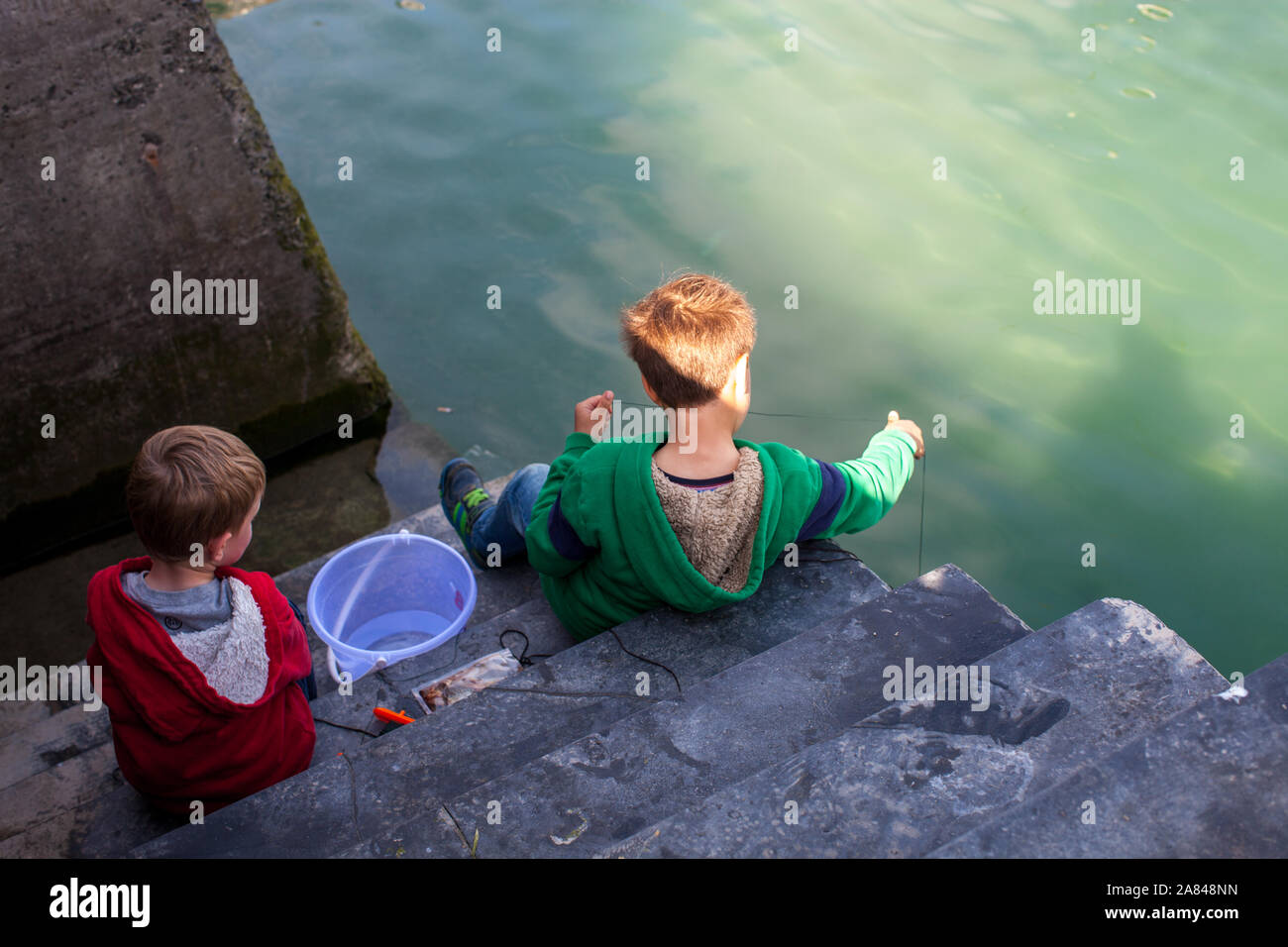Zwei Jungen krachen seitlich an einer Hafenmauer. Stockfoto