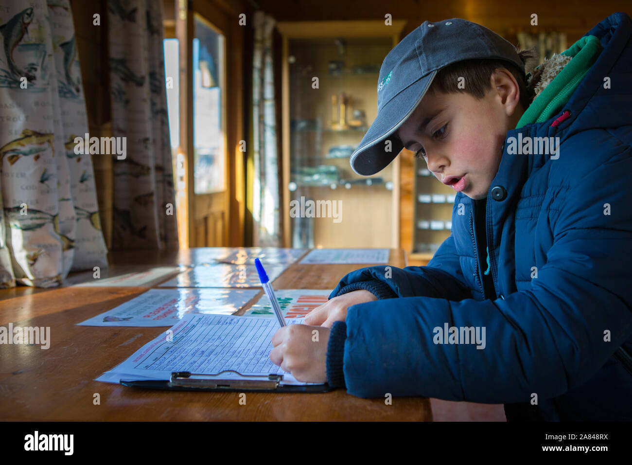 Ein kleiner Junge, der einen Bericht über die Fänge an einem Angelsee, Manningford Trout Fishery, Großbritannien, ausfüllt. Stockfoto