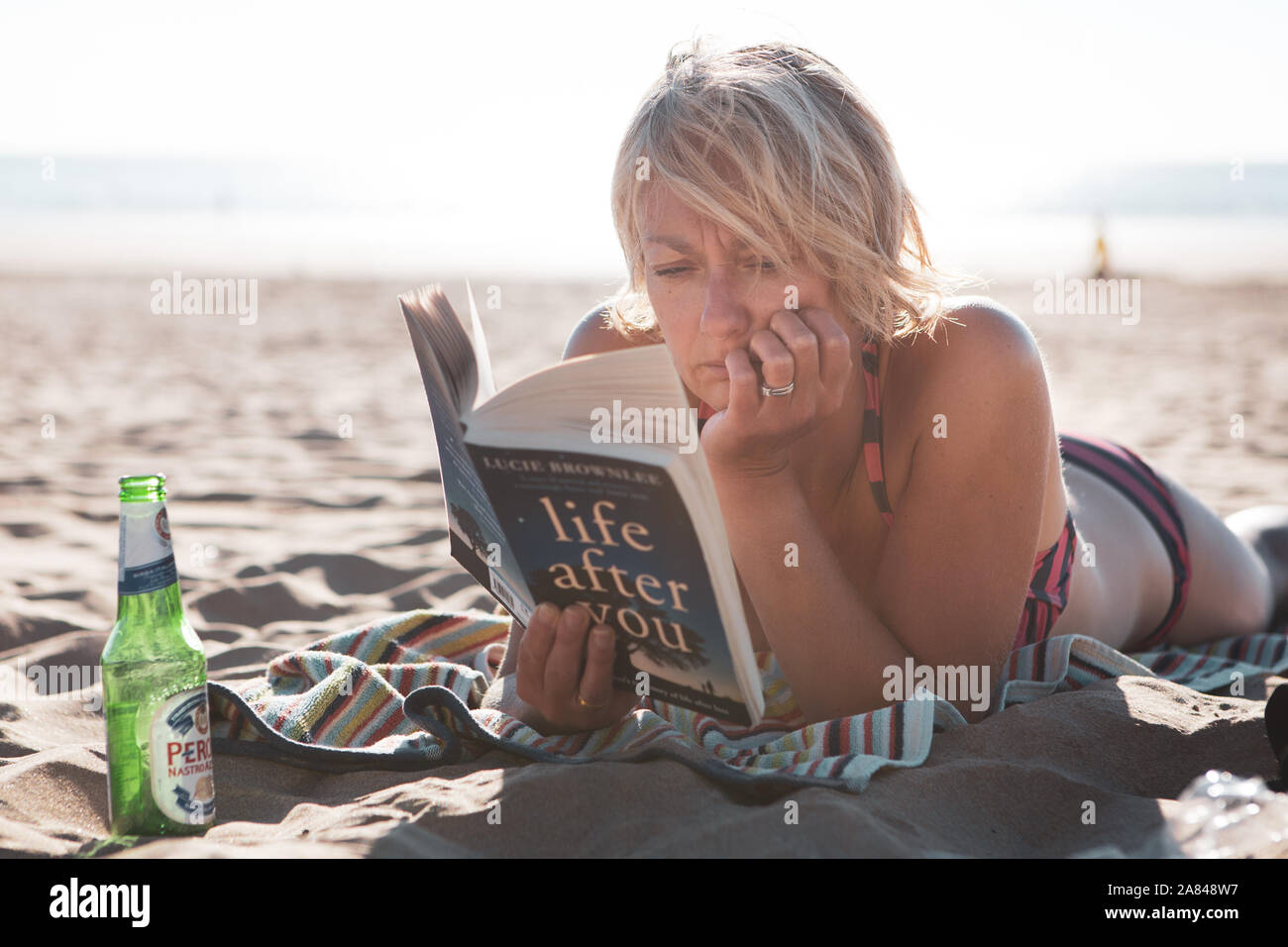 Eine junge Frau, die im Sommer ein Buch am Strand liest, Großbritannien. Stockfoto