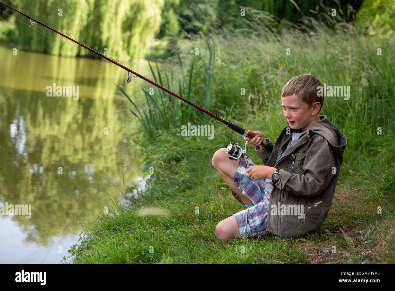 Ein kleiner Junge, der seine Angelrute neben einem See hält. Stockfoto