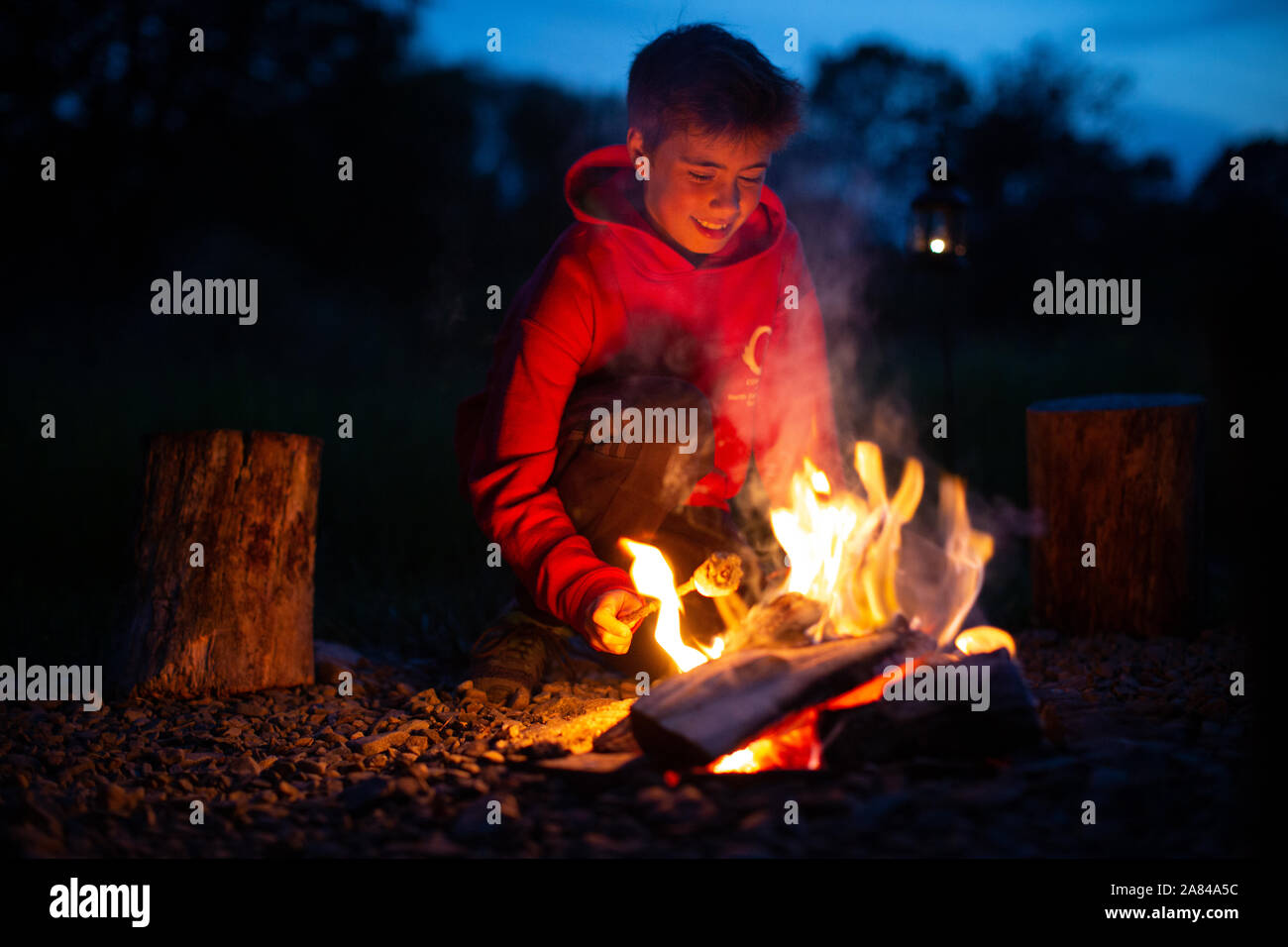 Ein kleiner Junge lächelt, während er beim Campen Marshmallows auf einem offenen Feuer kocht. Stockfoto